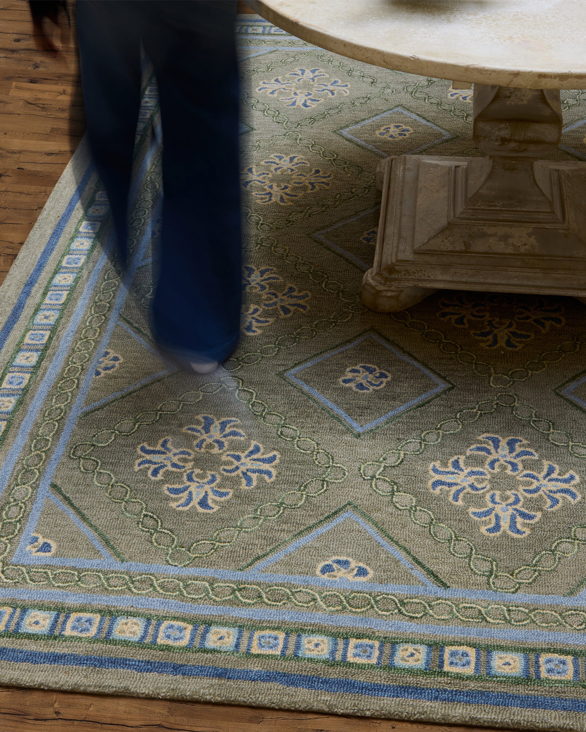 Patterned green and blue Varuna rug with a wooden table corner.