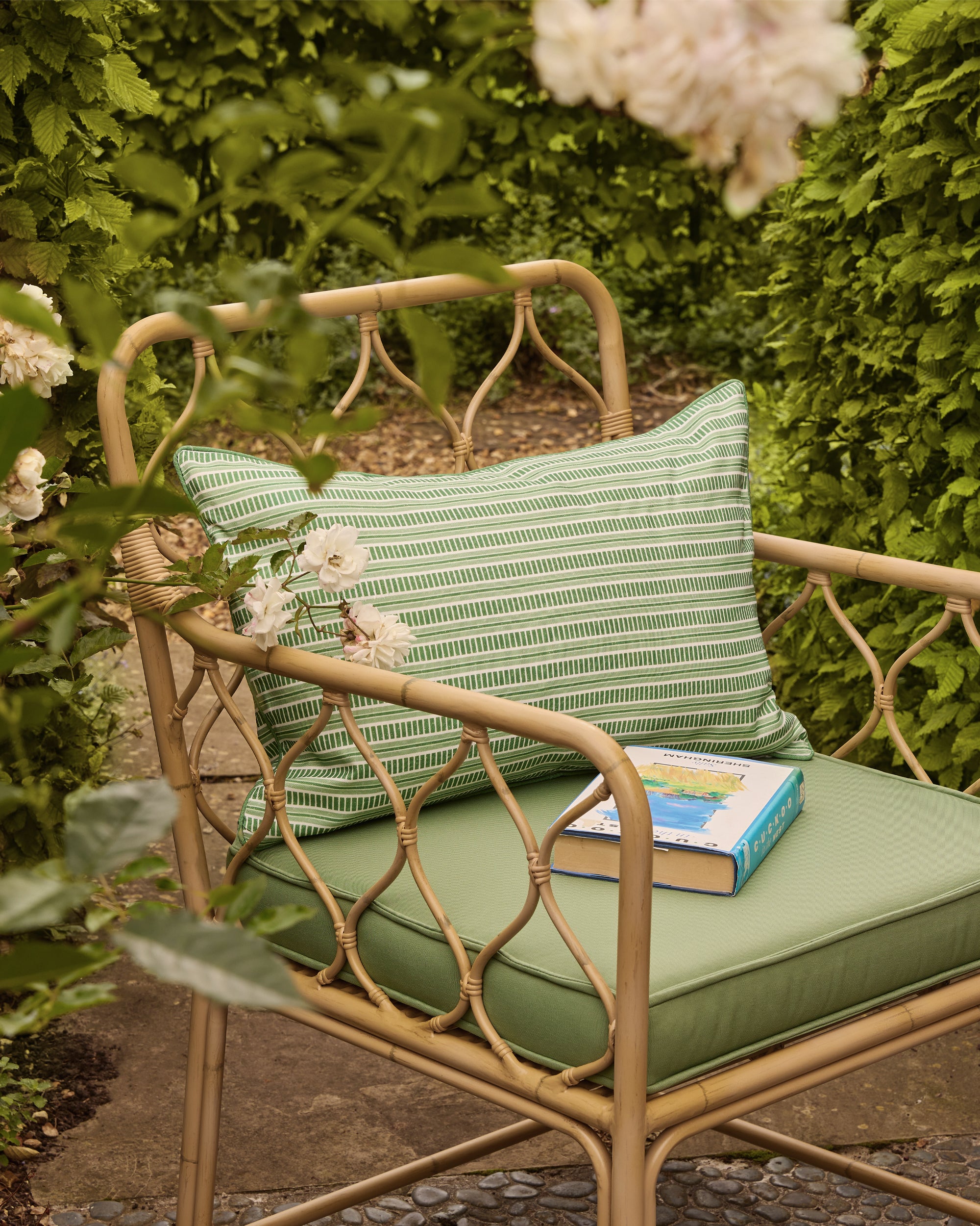 Wicker chair with green cushions and a striped pillow in a garden setting
