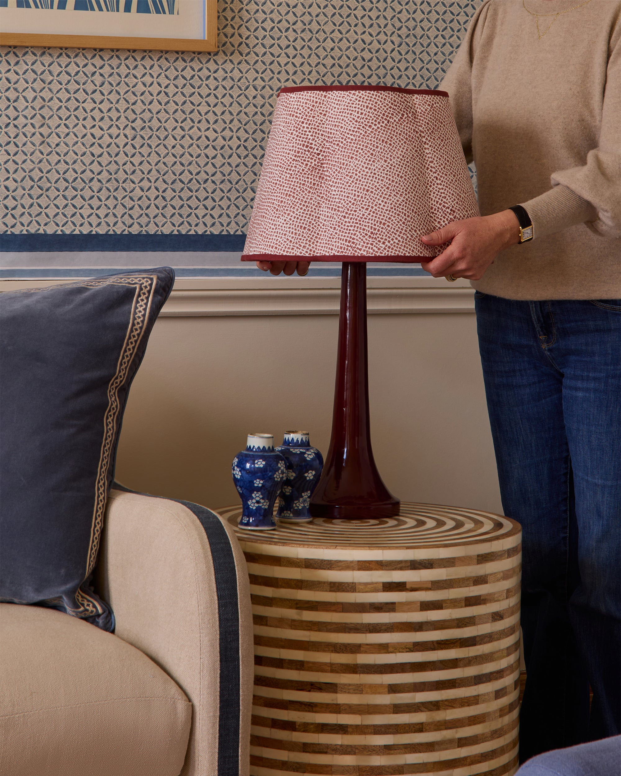 Person adjusting a lamp on a wooden side table in a living room.