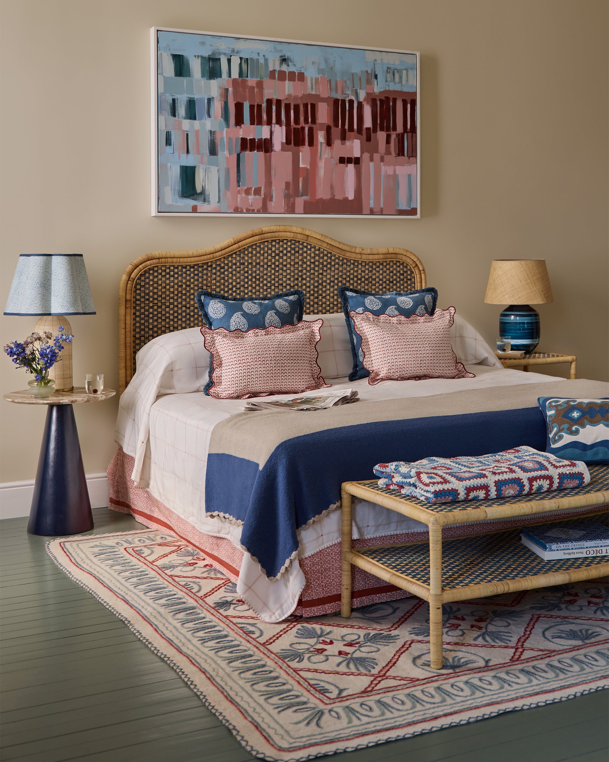 Bedroom with blue rattan headboard, colourful bedding, and abstract painting on wall.