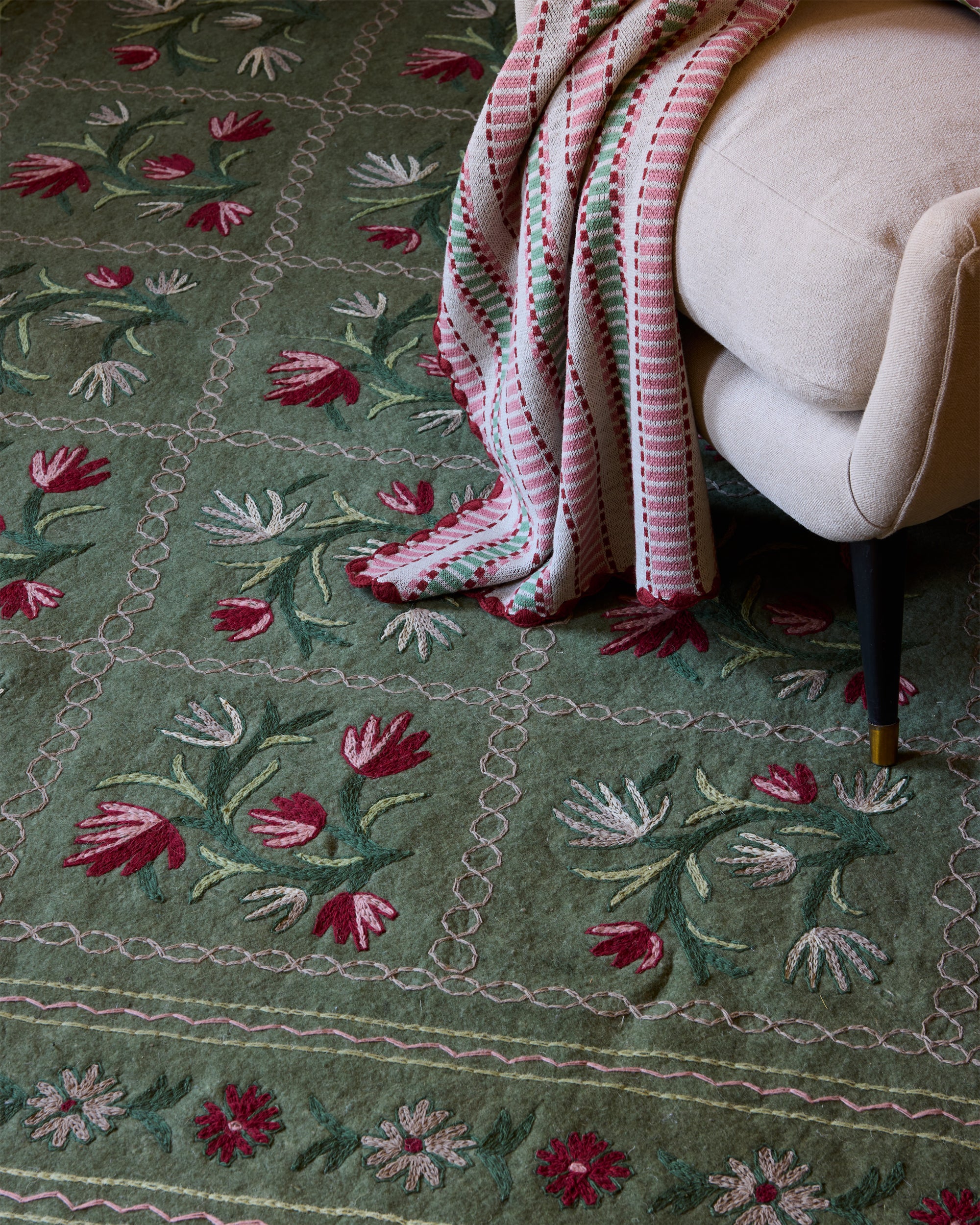 Embroidered green rug with floral patterns and a striped pink and white blanket draped over a chair.