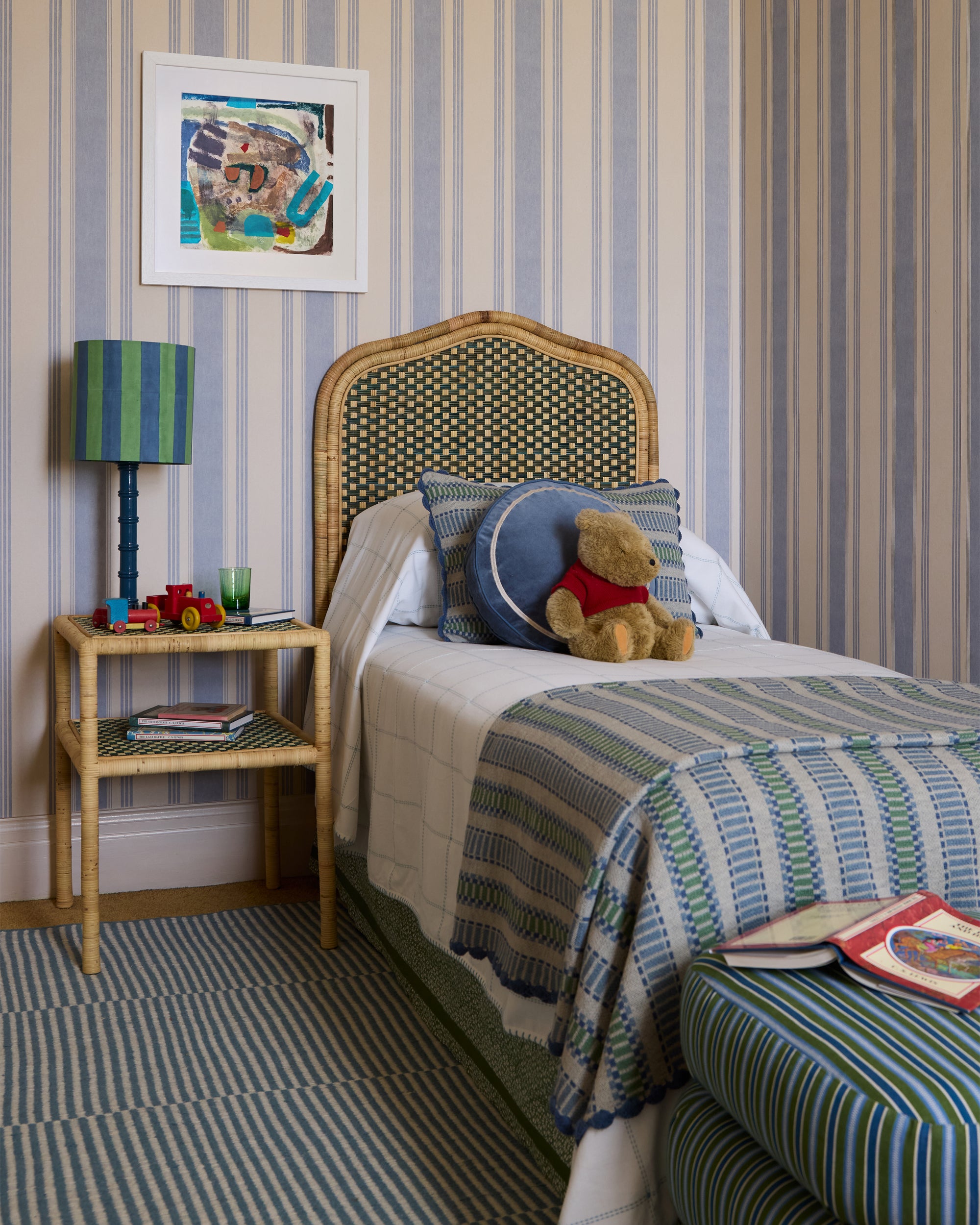 Children's bedroom with striped wallpaper, bed with teddy bear and pillows, and a nightstand with toys.