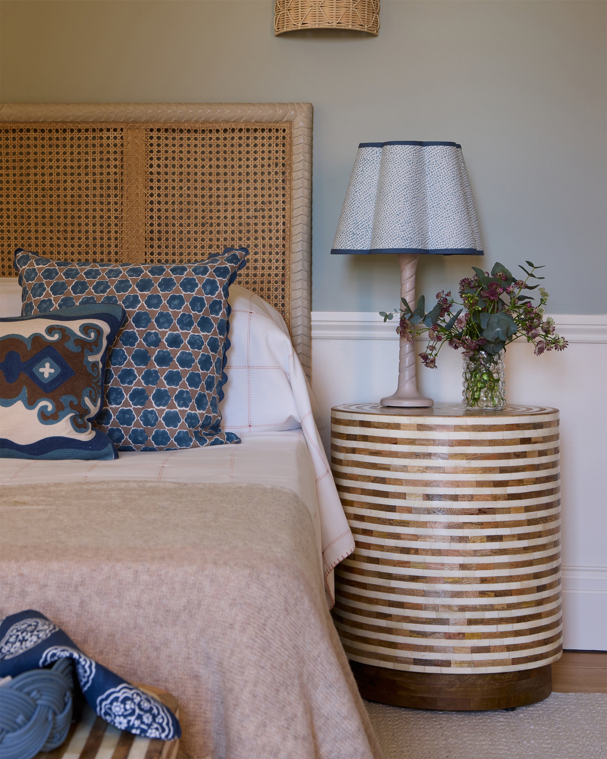 Bedroom with wicker headboard and side table, featuring decorative pillows and a lamp.