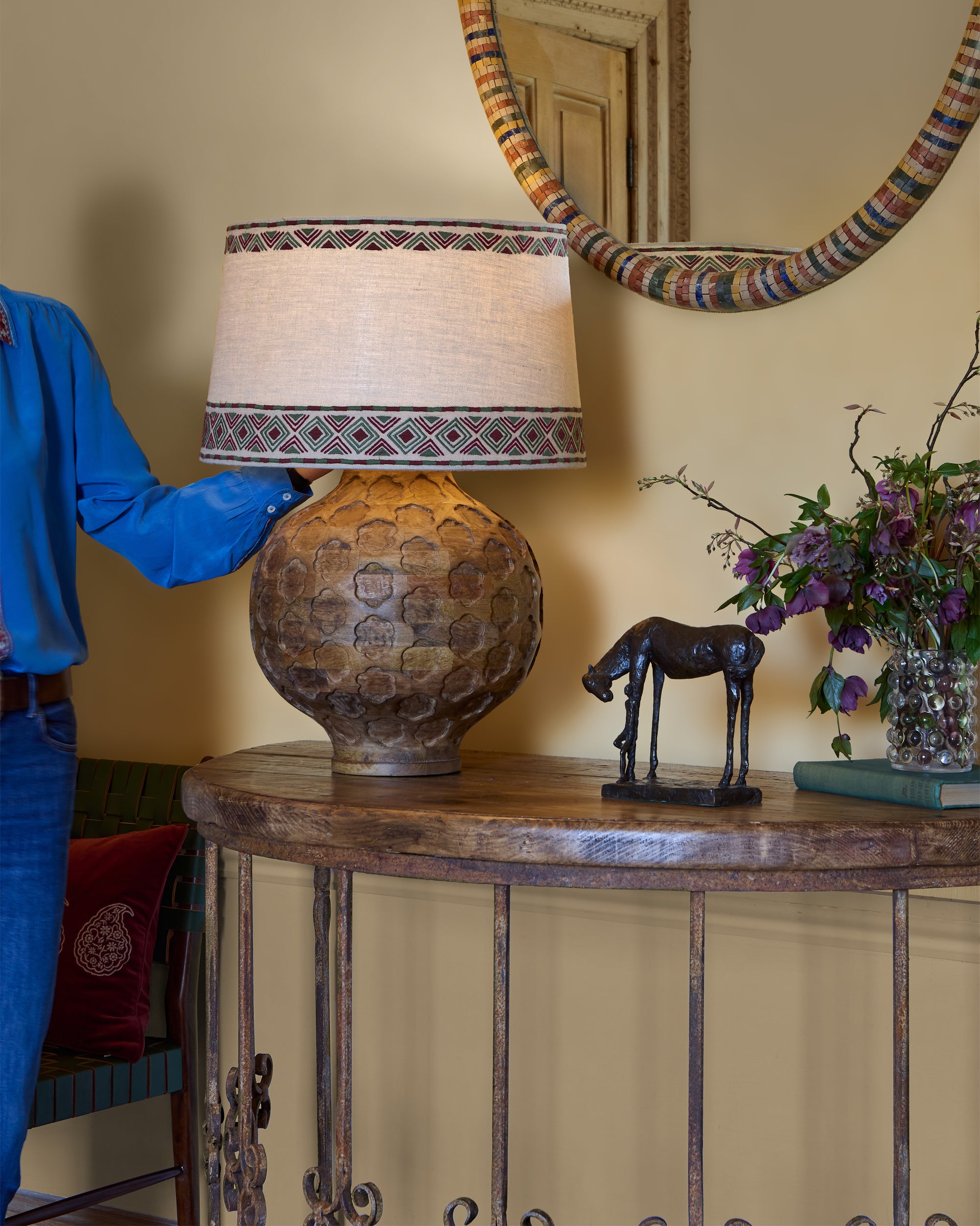 Person adjusting a lamp on a decorative table with a mirror and vase in the background.