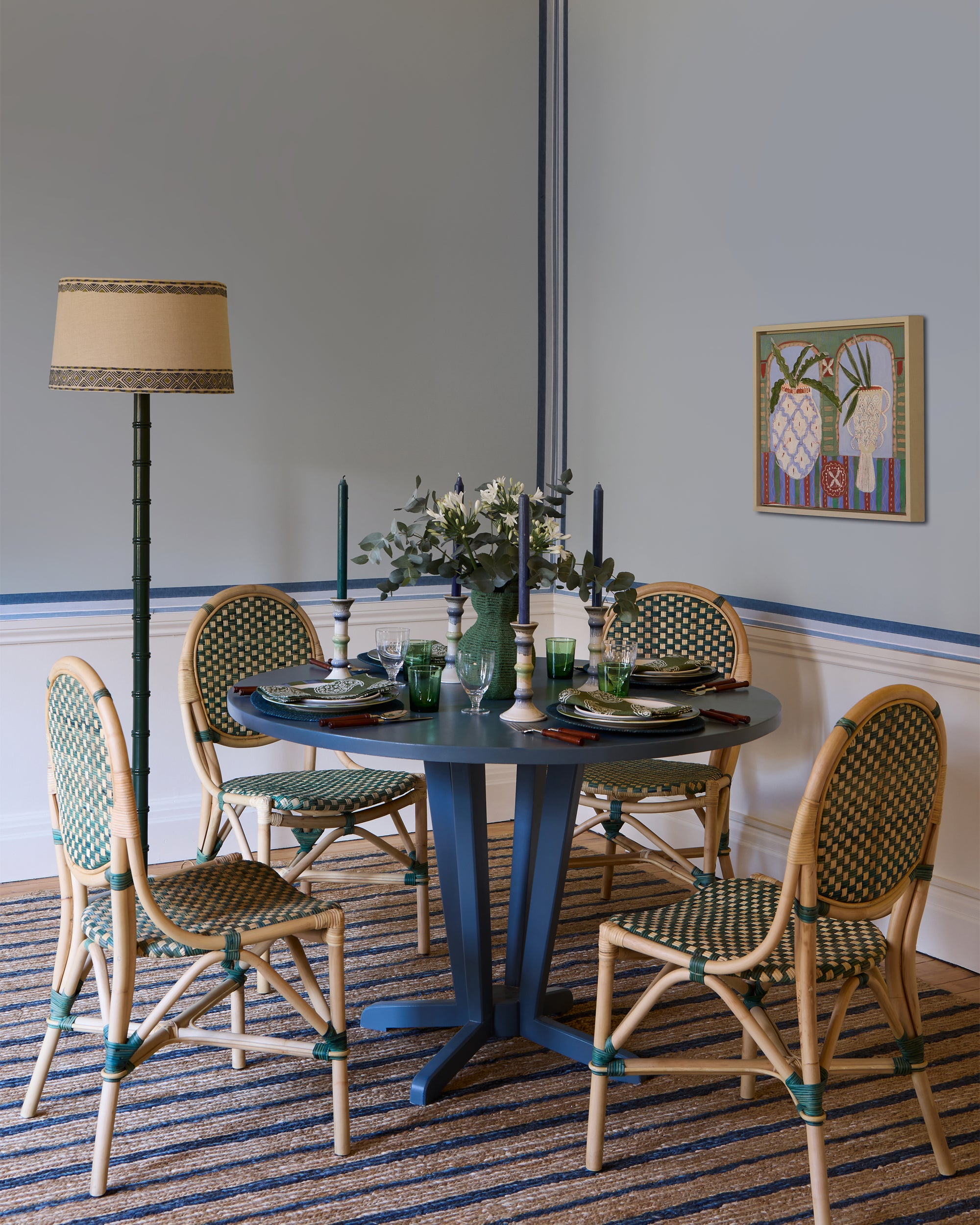 Dining room with a blue table and wicker chairs, featuring a lamp and artwork on the wall.