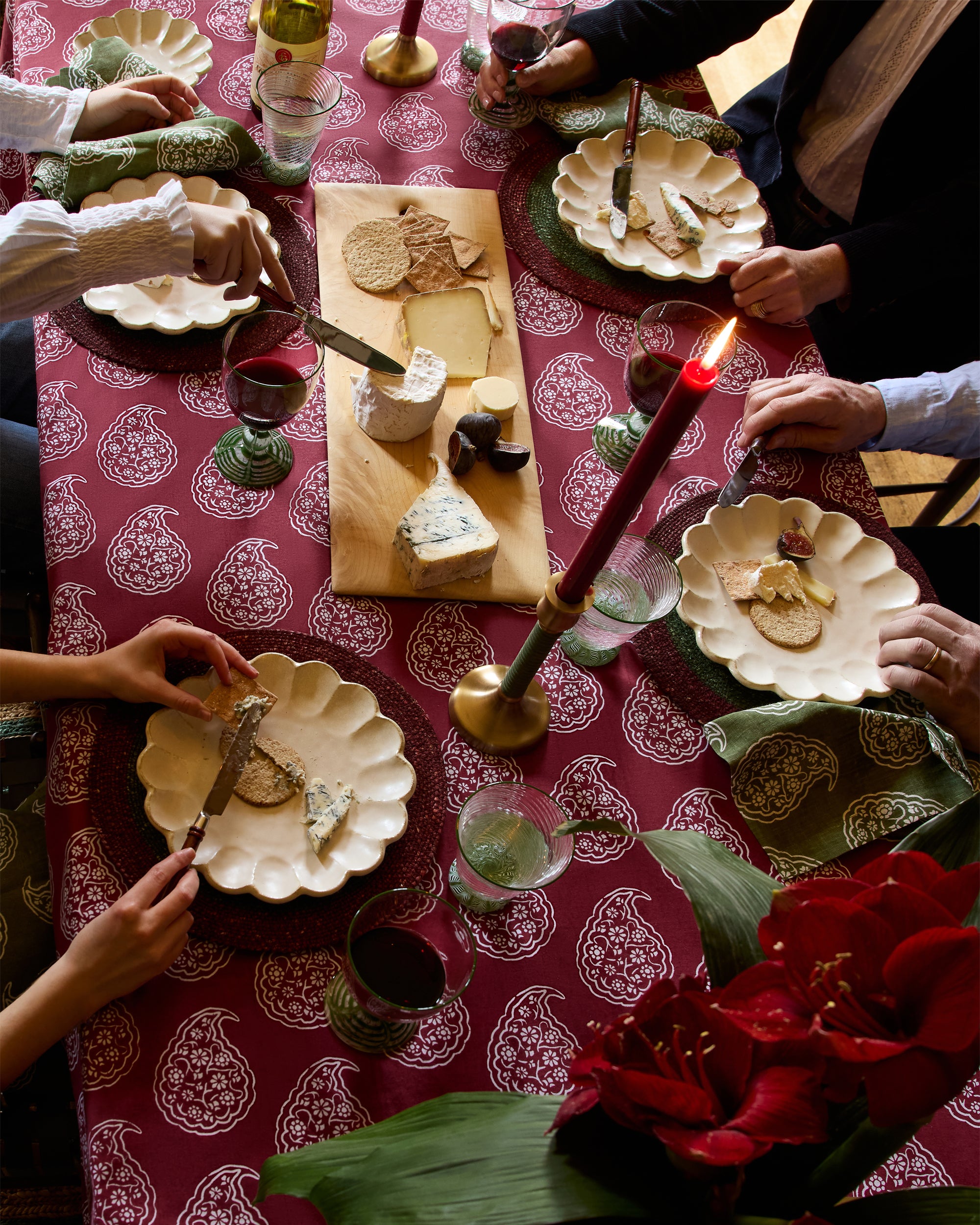 People enjoying a meal around a table with a red patterned tablecloth, candles, and various dishes.