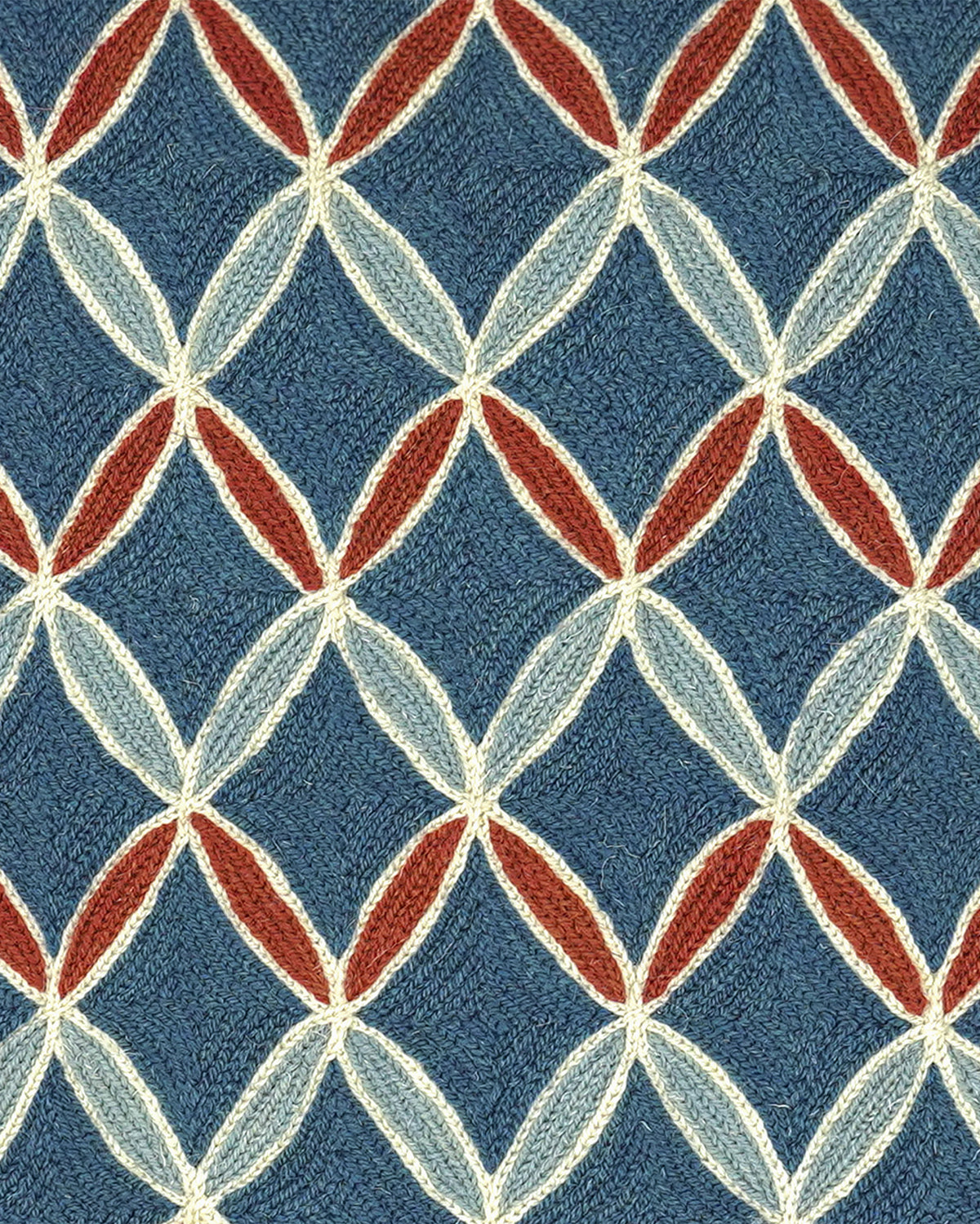 A close-up of a woven fabric pattern featuring a repeating geometric diamond design in slate blue, cream, light blue, and rust red.