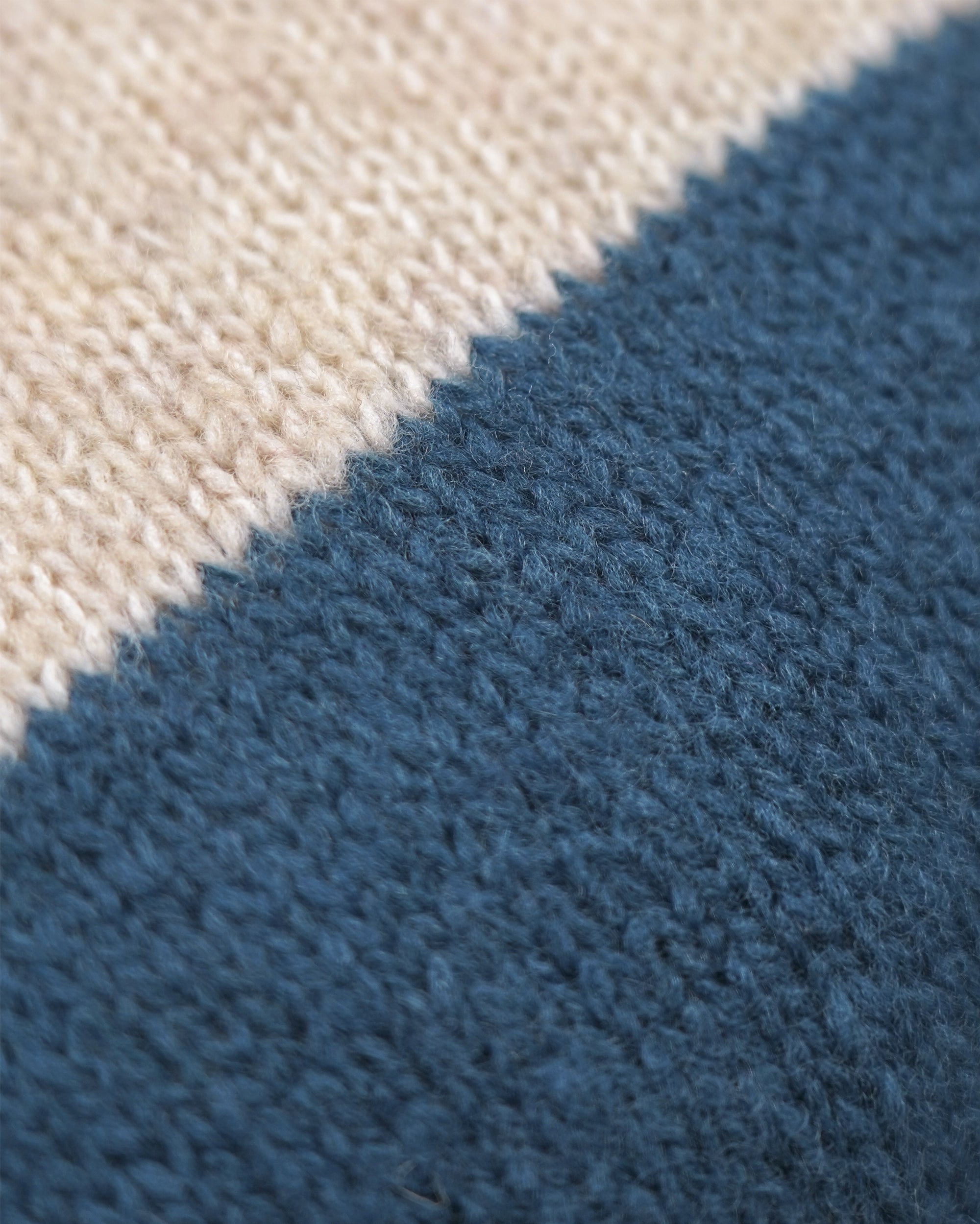 Close-up of a textured knit fabric with a diagonal color-block pattern in cream and slate blue.