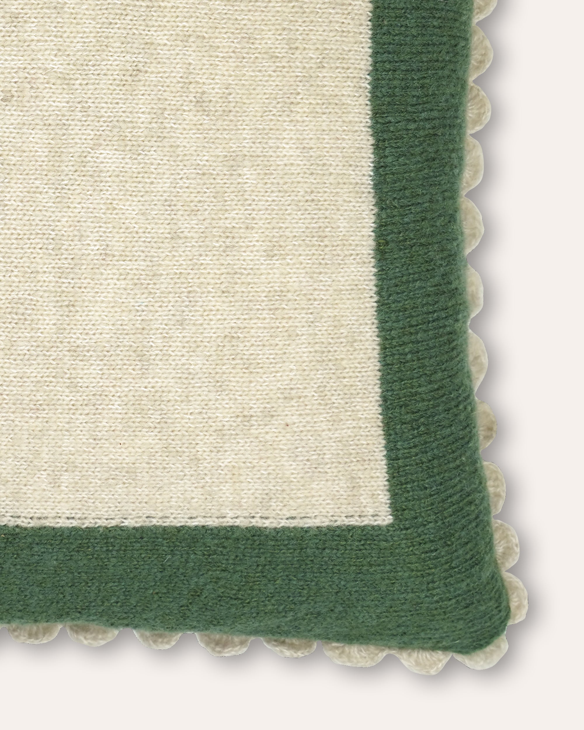 Close-up of a woven textile corner showing a cream center field bordered by a dark green knitted border with a scalloped edge.