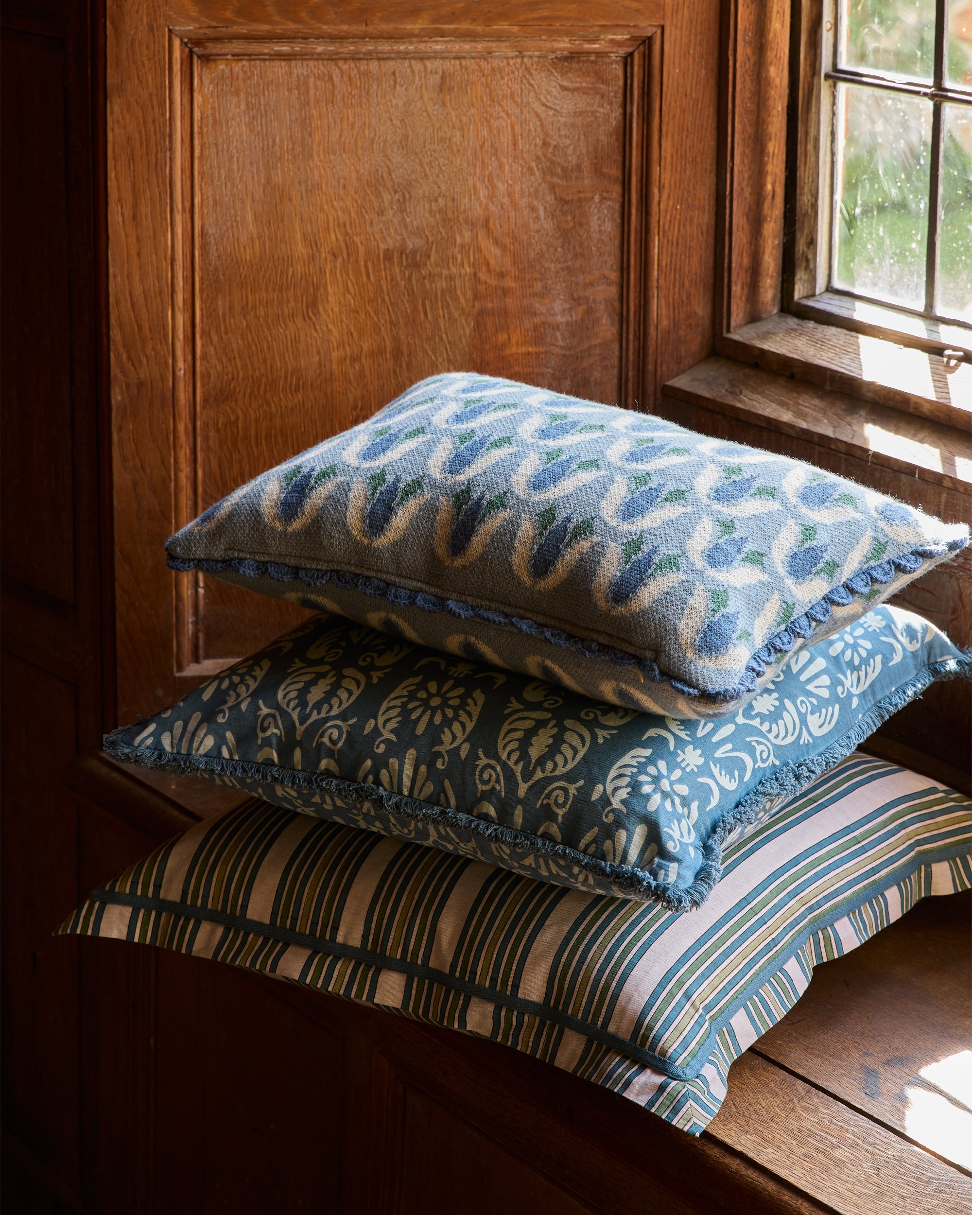 Stack of decorative cushions with blue and green patterns on a wooden surface.