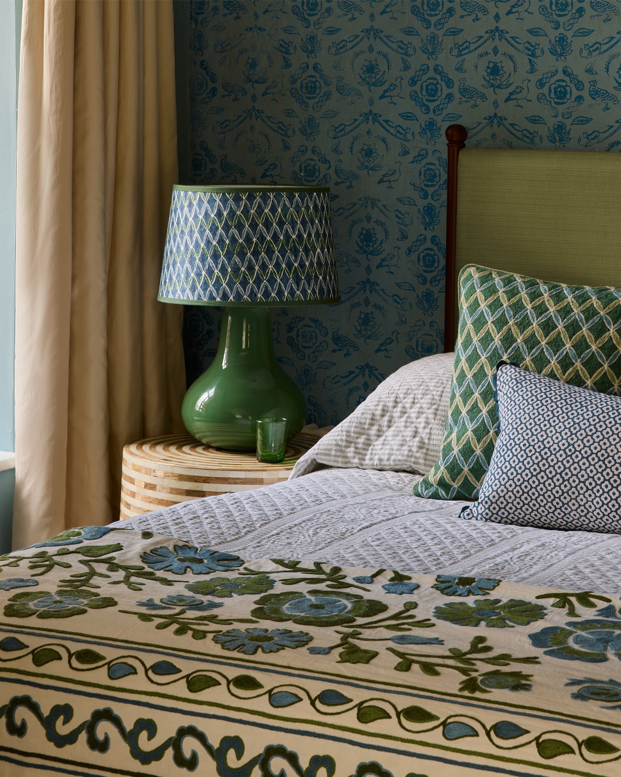 Bedroom with floral bedspread, green lamp, and patterned headboard.