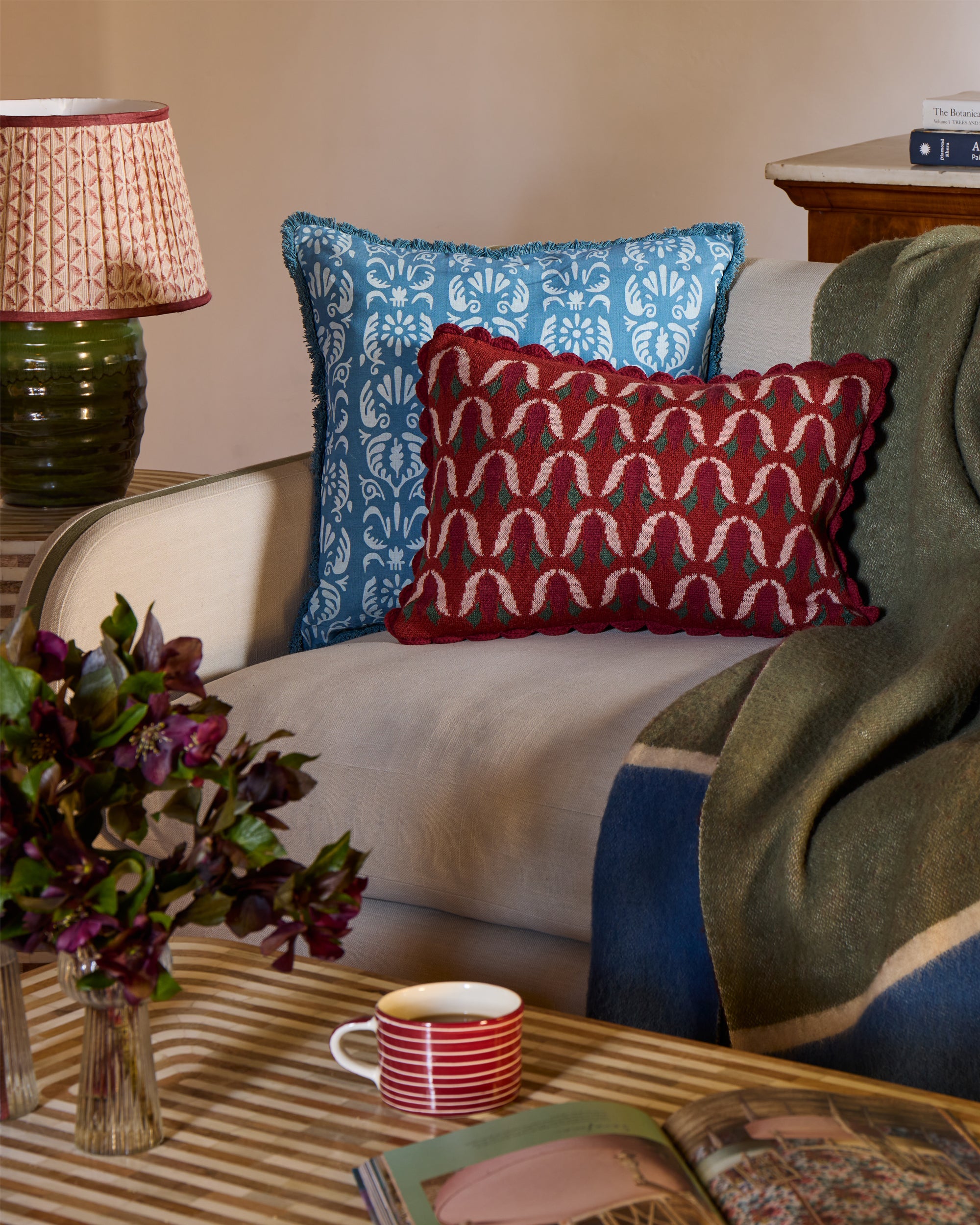 Decorative cushions on a sofa with a lamp, coffee cup, and flowers in the foreground.