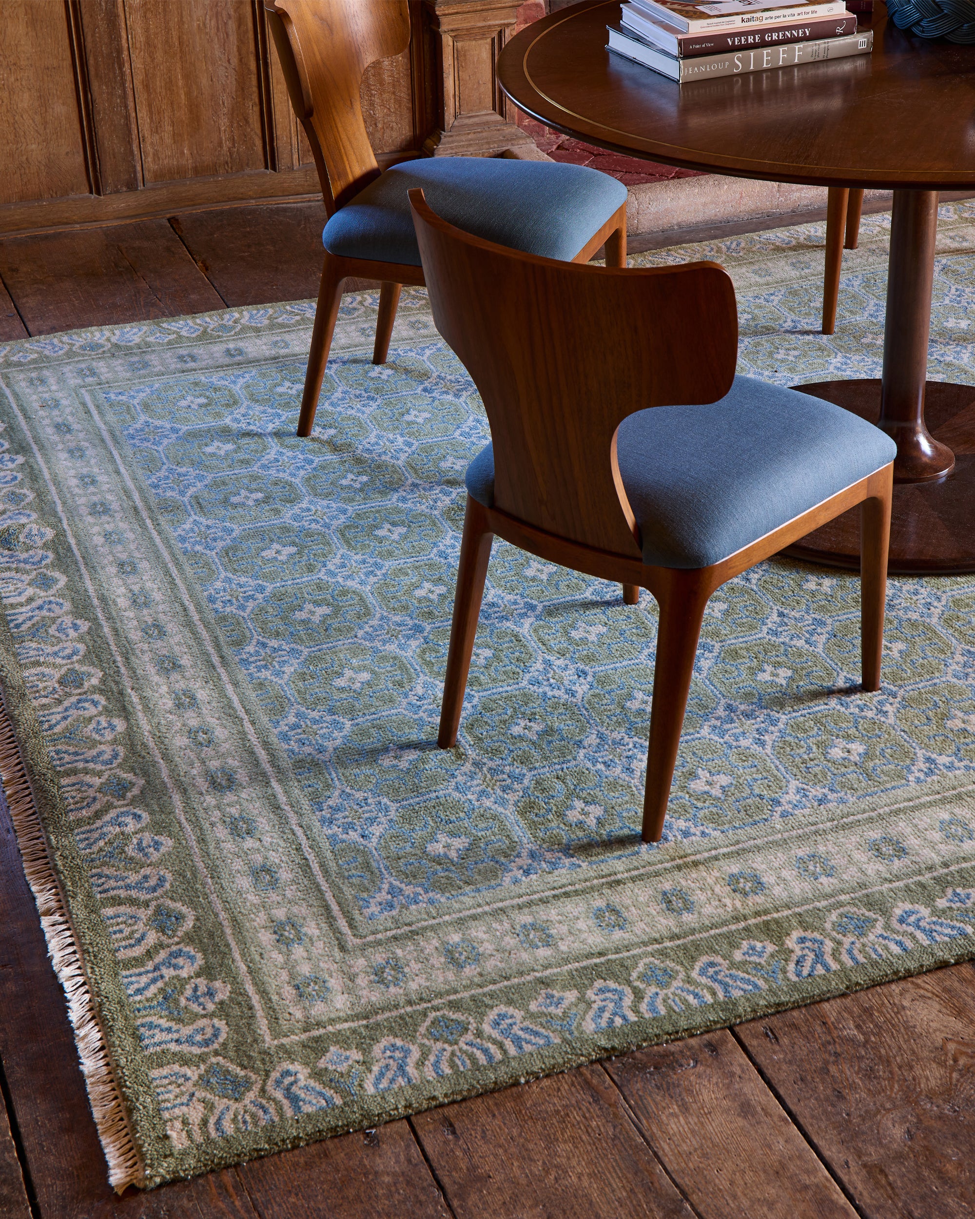 Decorative rug with intricate patterns on a wooden floor, chairs, and a table in the background.