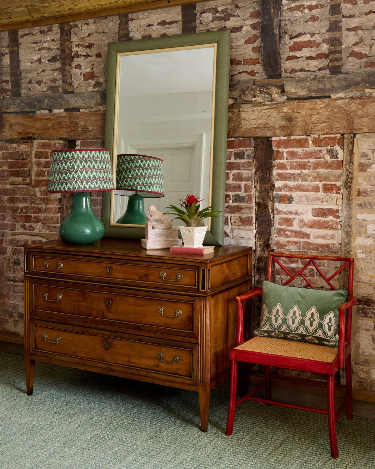 Wooden dresser with green lamps and a red chair against a brick wall.
