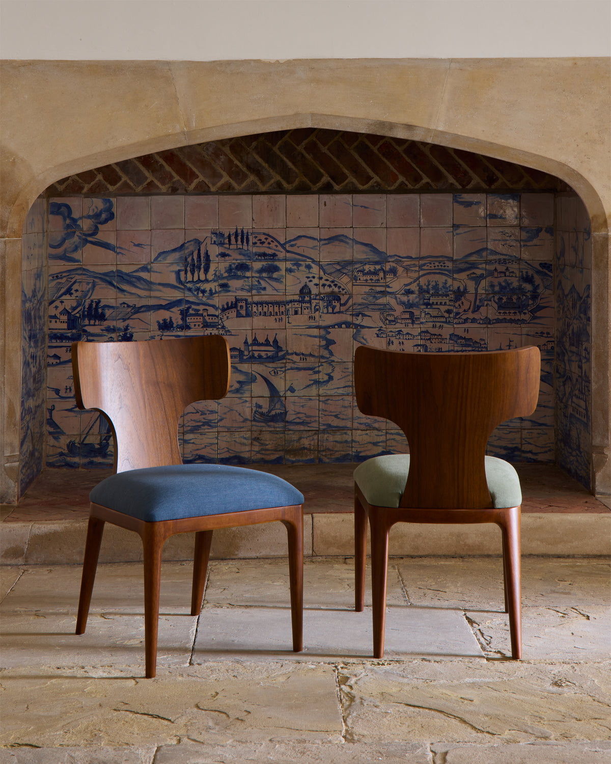 Two wooden chairs with upholstered seats in a room with tiled walls featuring a landscape design.