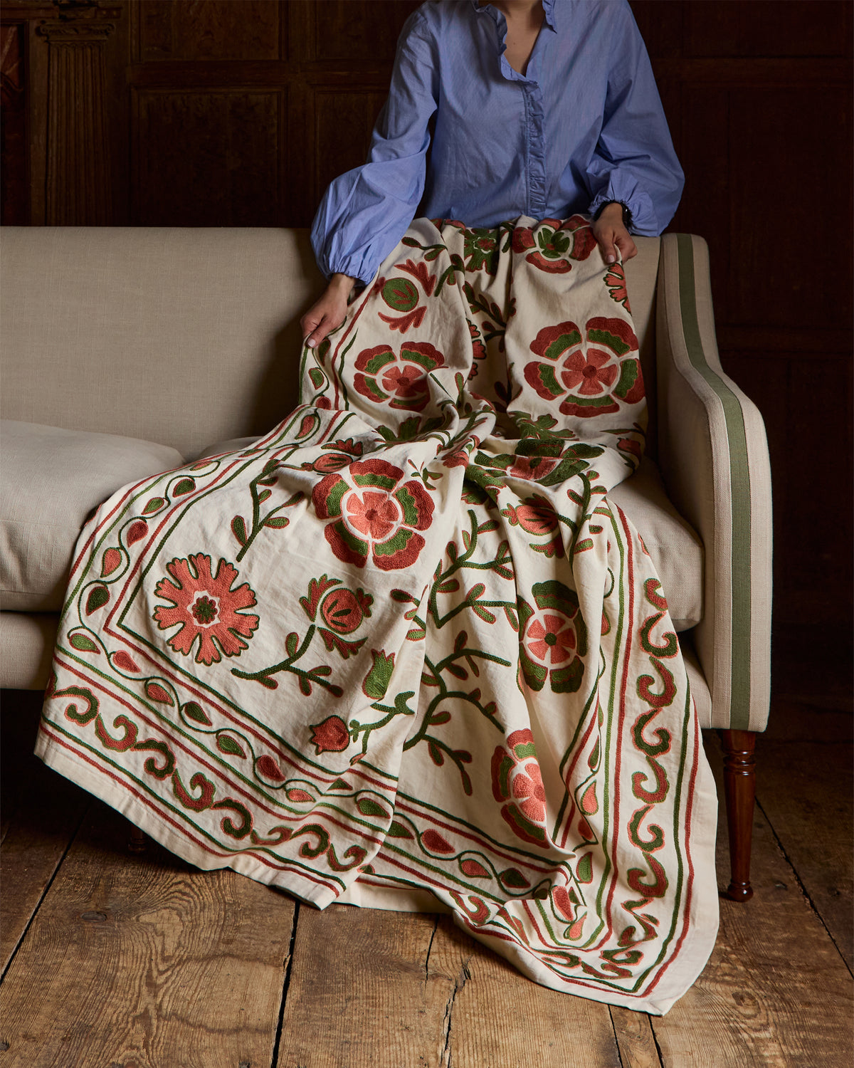 Person arranging a floral-patterned suzani throw on a sofa.