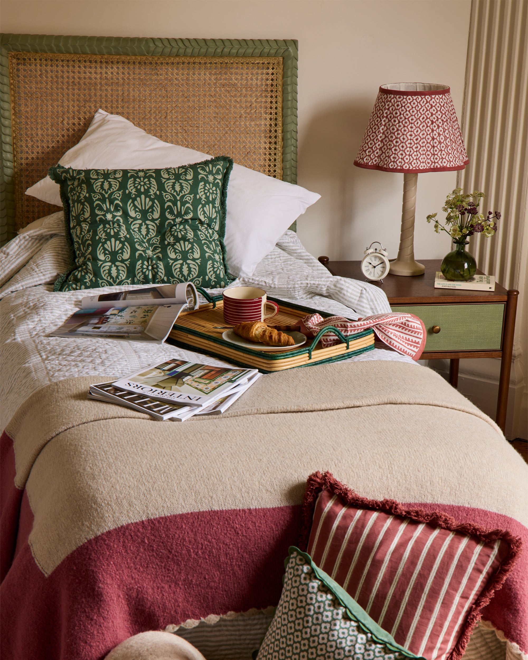 Cozy bedroom with a bed, pillows, a lamp, and a tray with food and drinks.