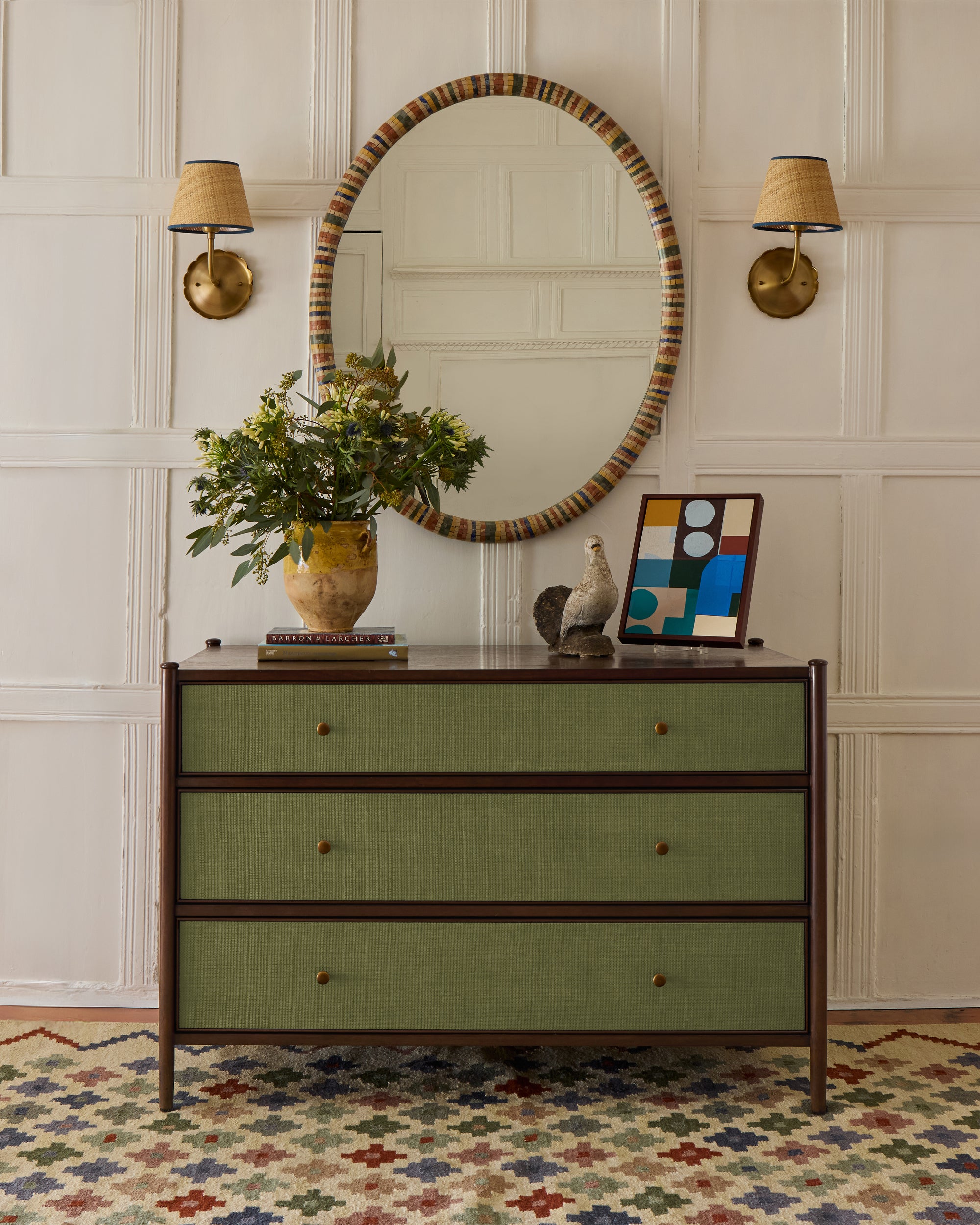 Green dresser with decorative items against a wall with wainscoting and a patterned rug.