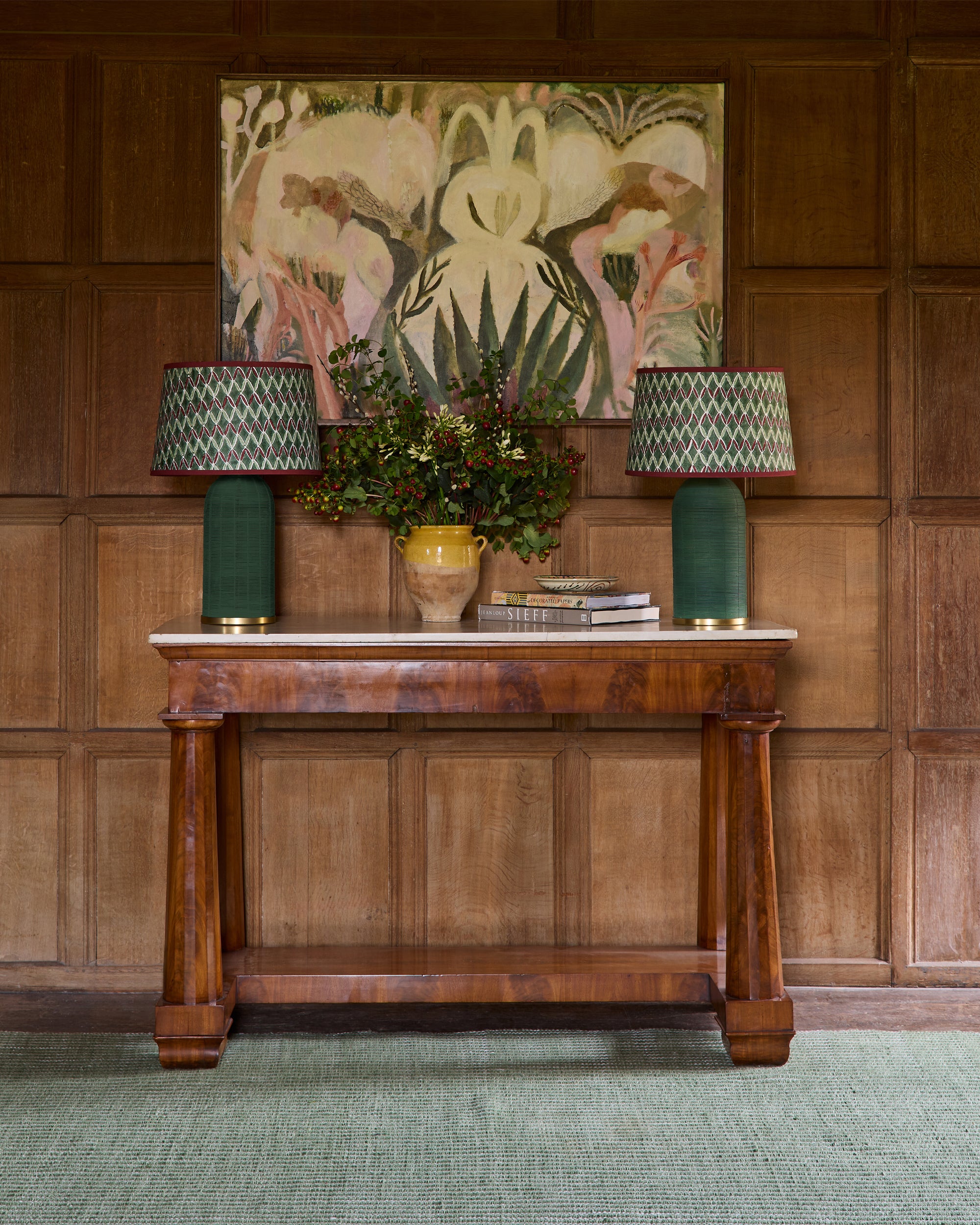Wooden console table with lamps and decorative items against a wooden wall with a painting.