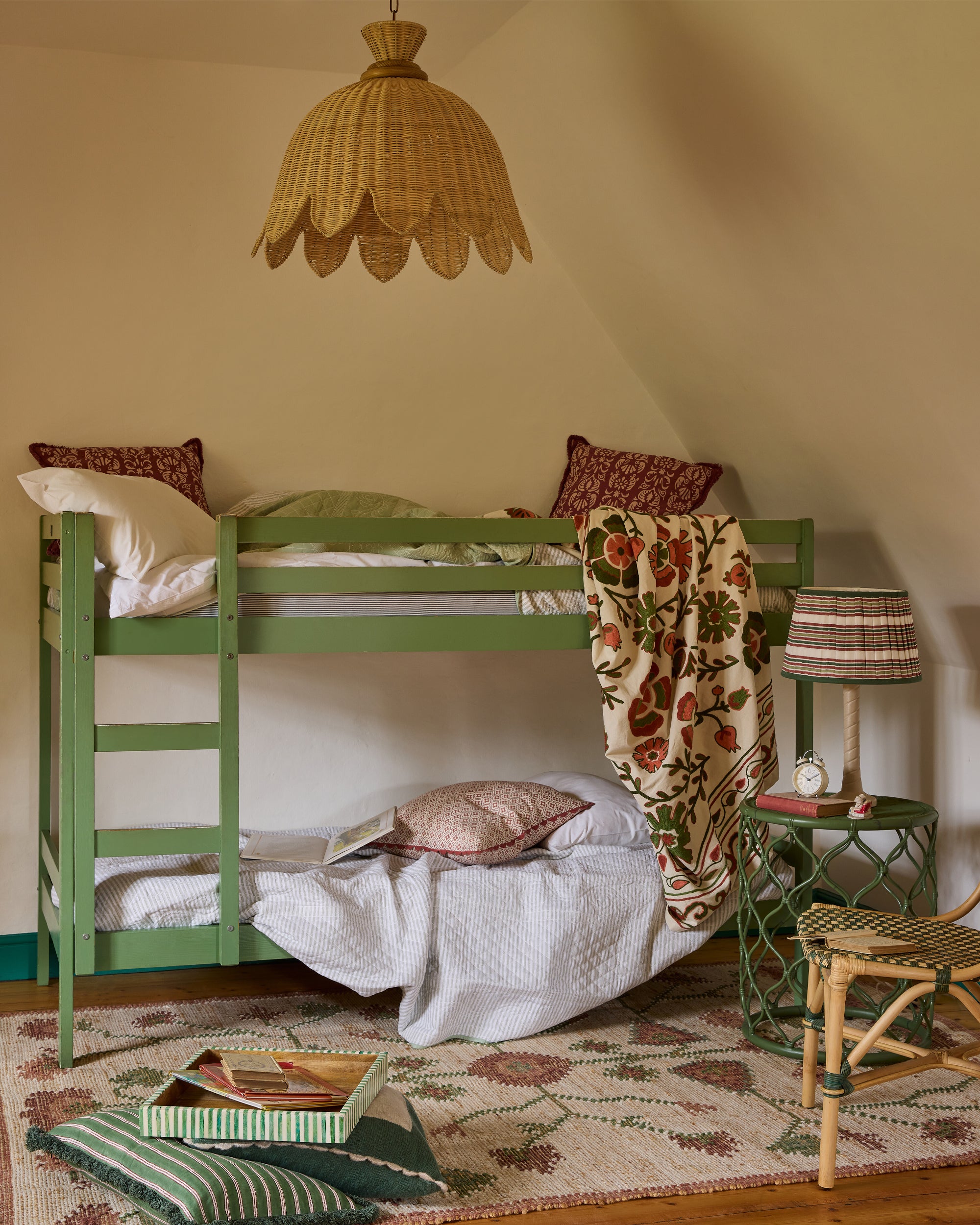 Green bunk bed with floral blanket in a cozy room with lamp and chair.