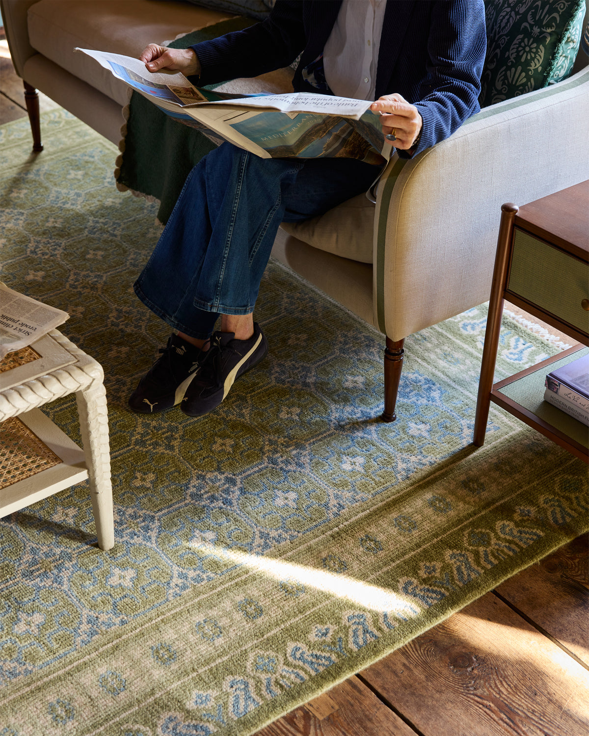 Person sitting on a chair reading a book in a room with a patterned rug.