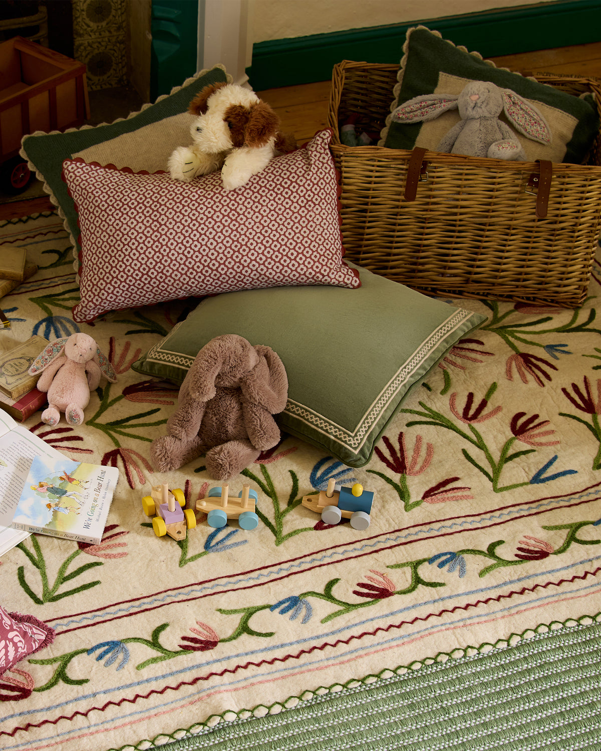 Children's room with toys, cushions, and a basket on a patterned rug.