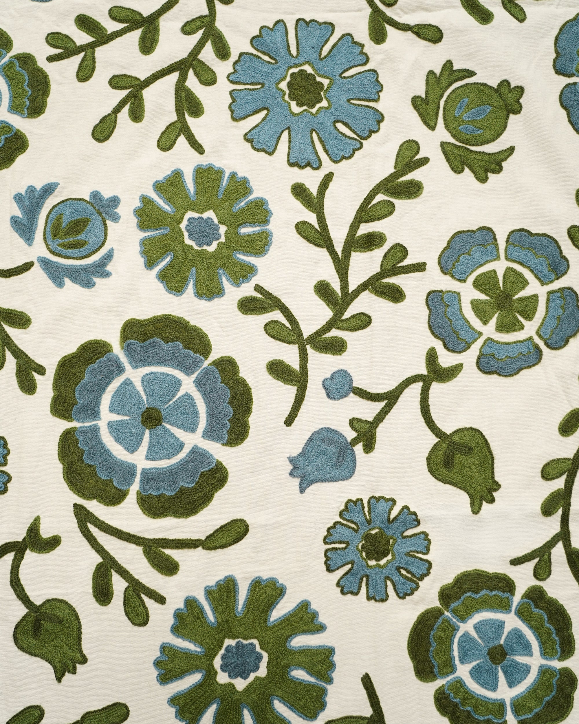 A close-up of a textile pattern featuring stylized blue and green flowers with leafy vines on an off-white background.