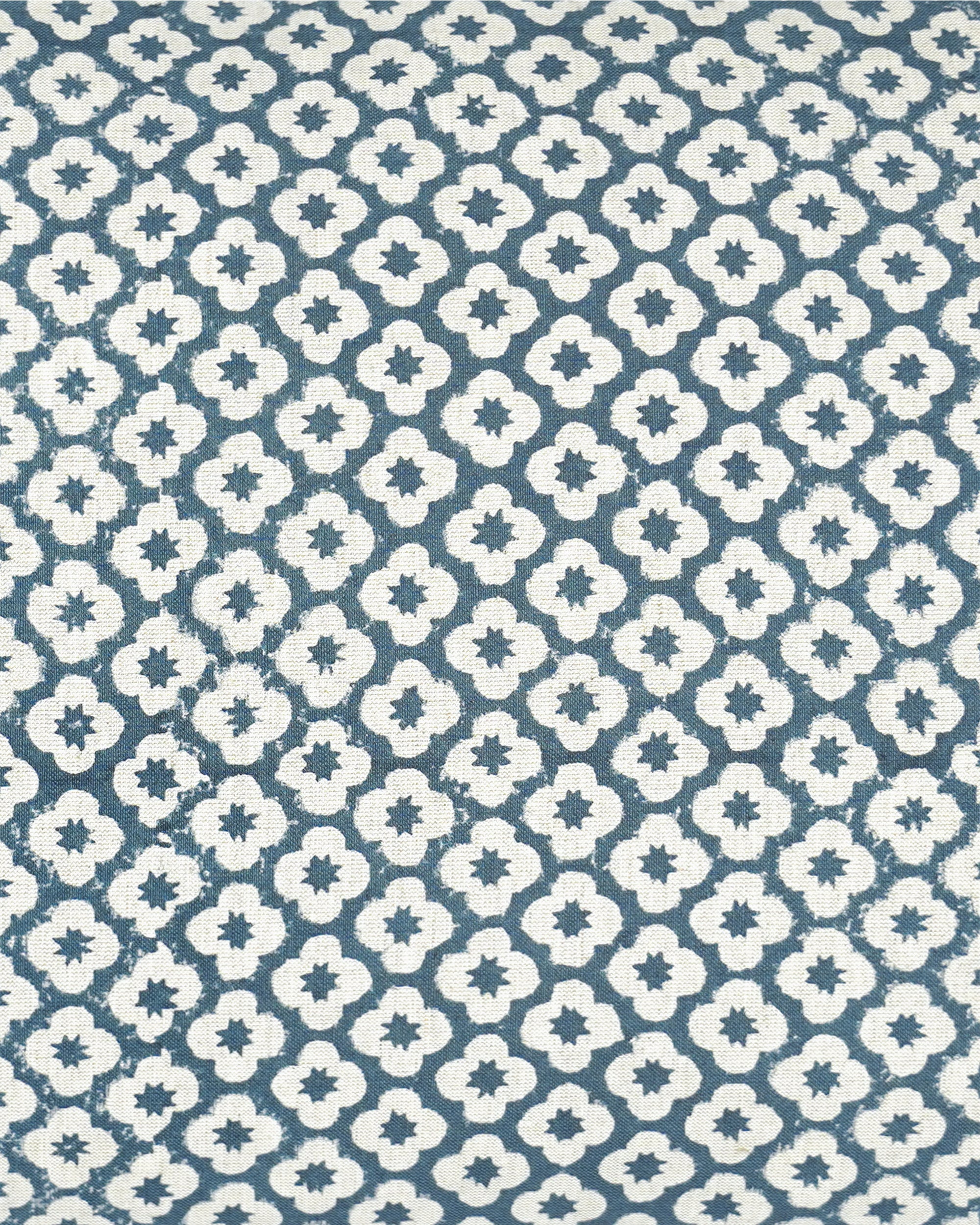 A close-up of a fabric pattern featuring a repeating white quatrefoil and star motif on a muted slate blue background.