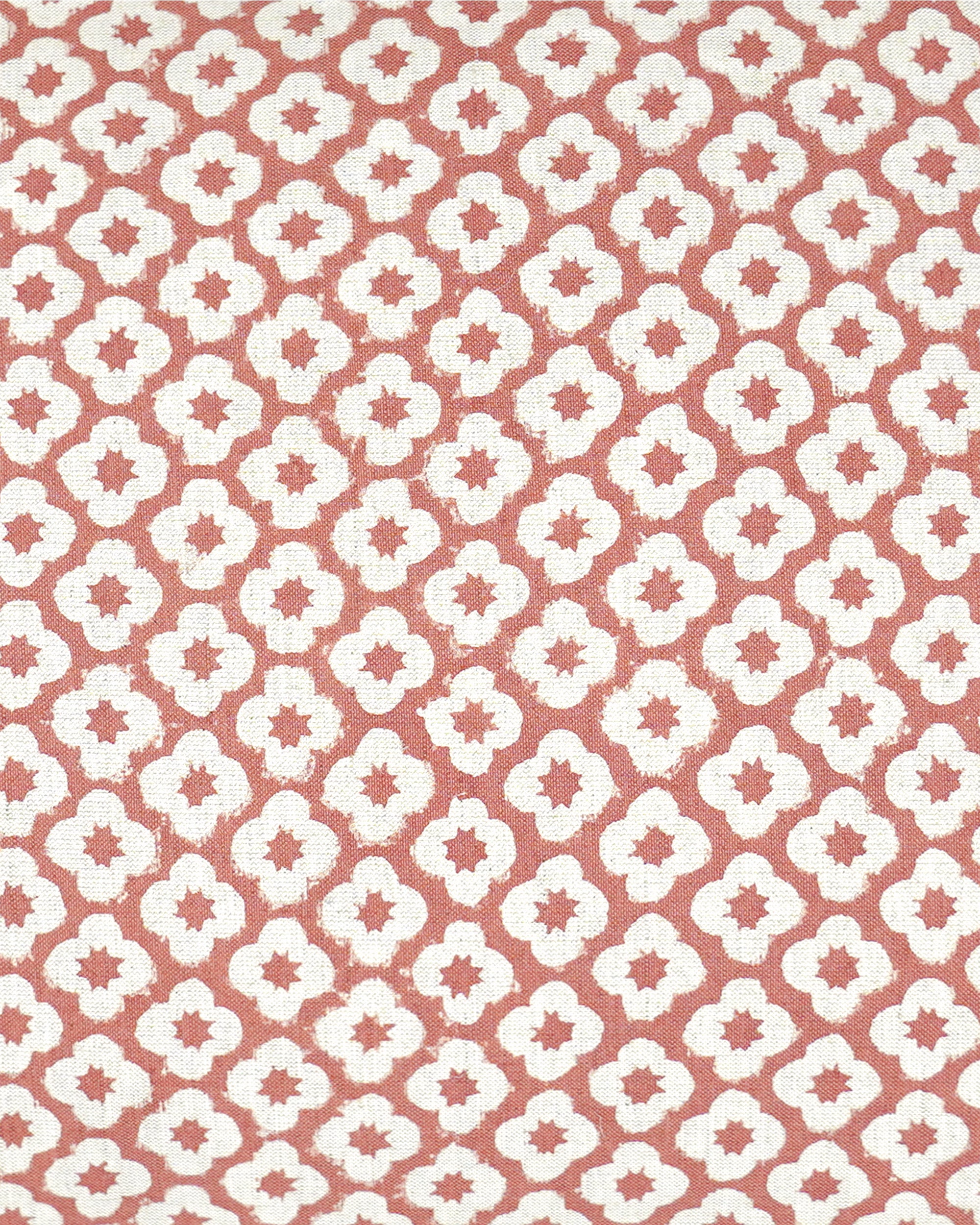 A close-up of a repeating fabric pattern featuring white quatrefoil-like motifs on a muted terracotta pink background.