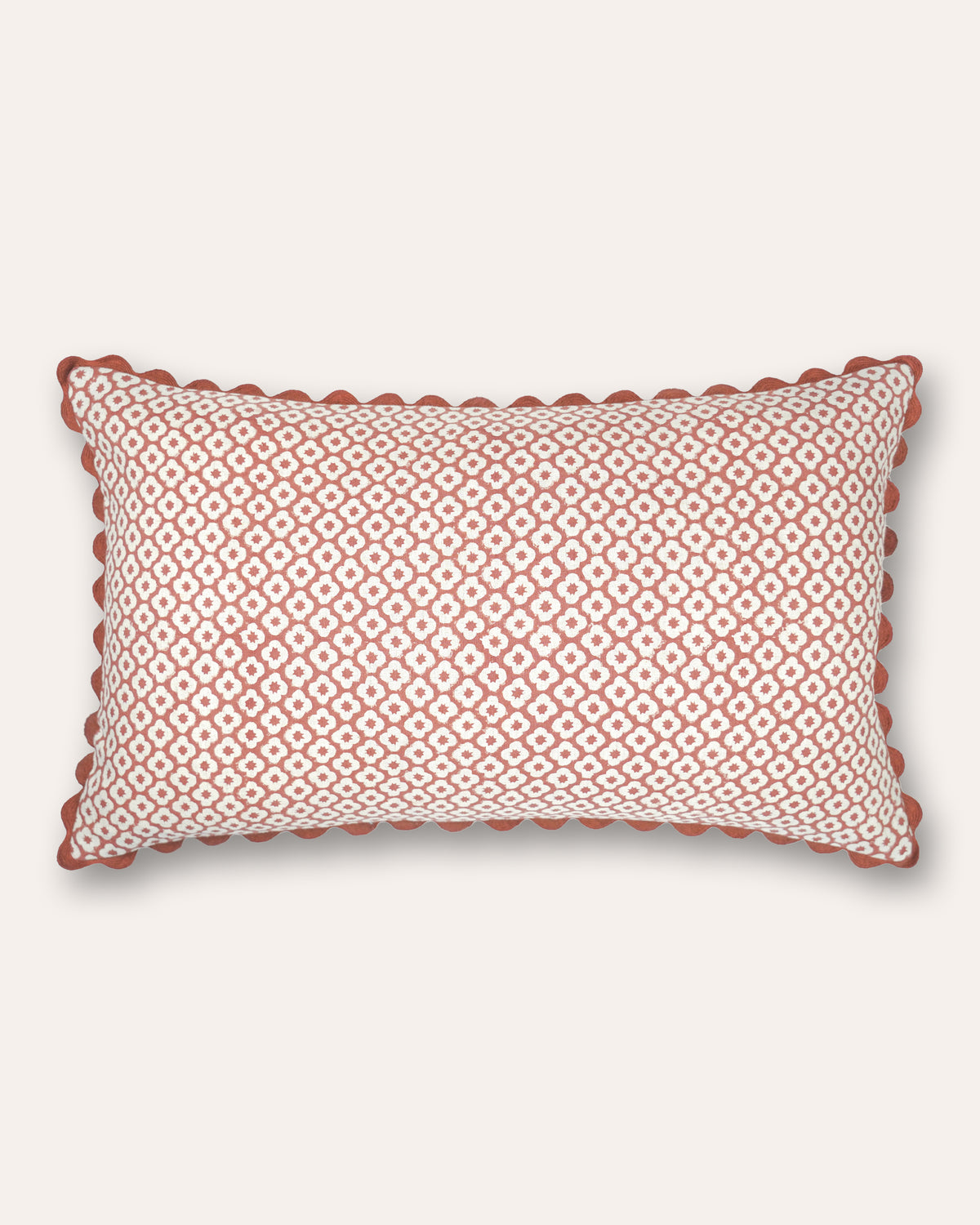 A rectangular cushion featuring a repeating geometric diamond pattern in terracotta and off-white, finished with a scalloped terracotta border, shown against a light cream background.
