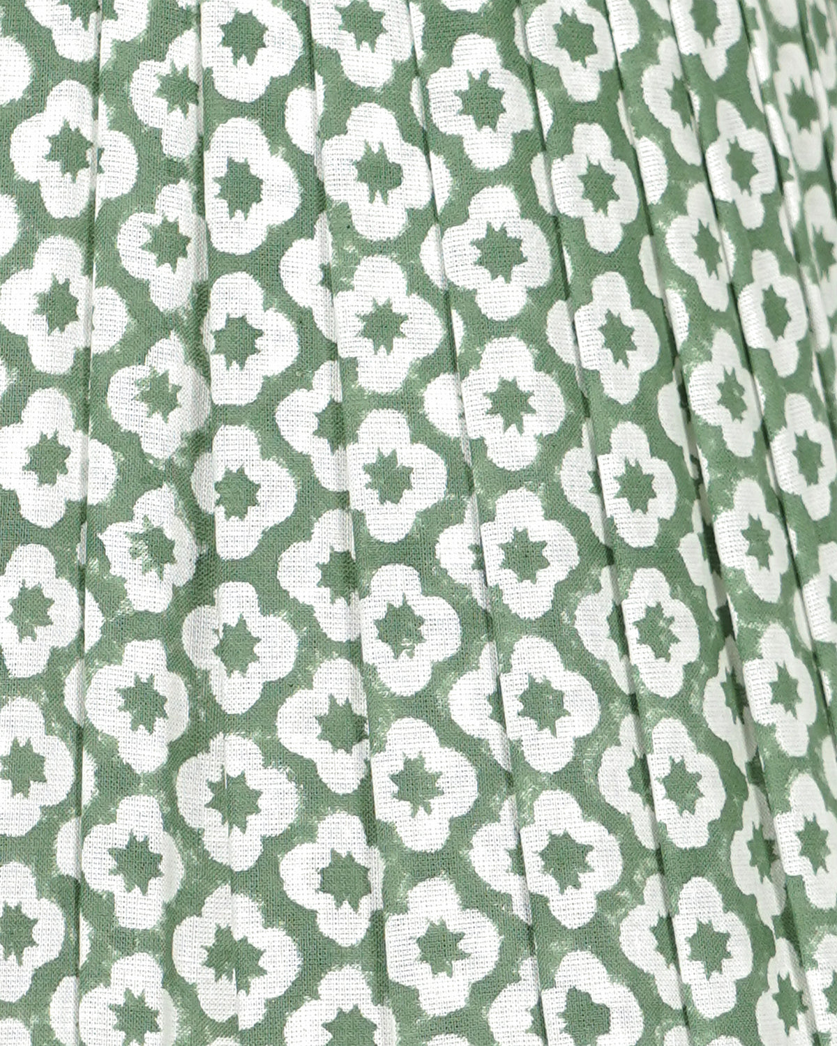 A close-up of a pleated fabric with a repeating green and white geometric quatrefoil pattern.
