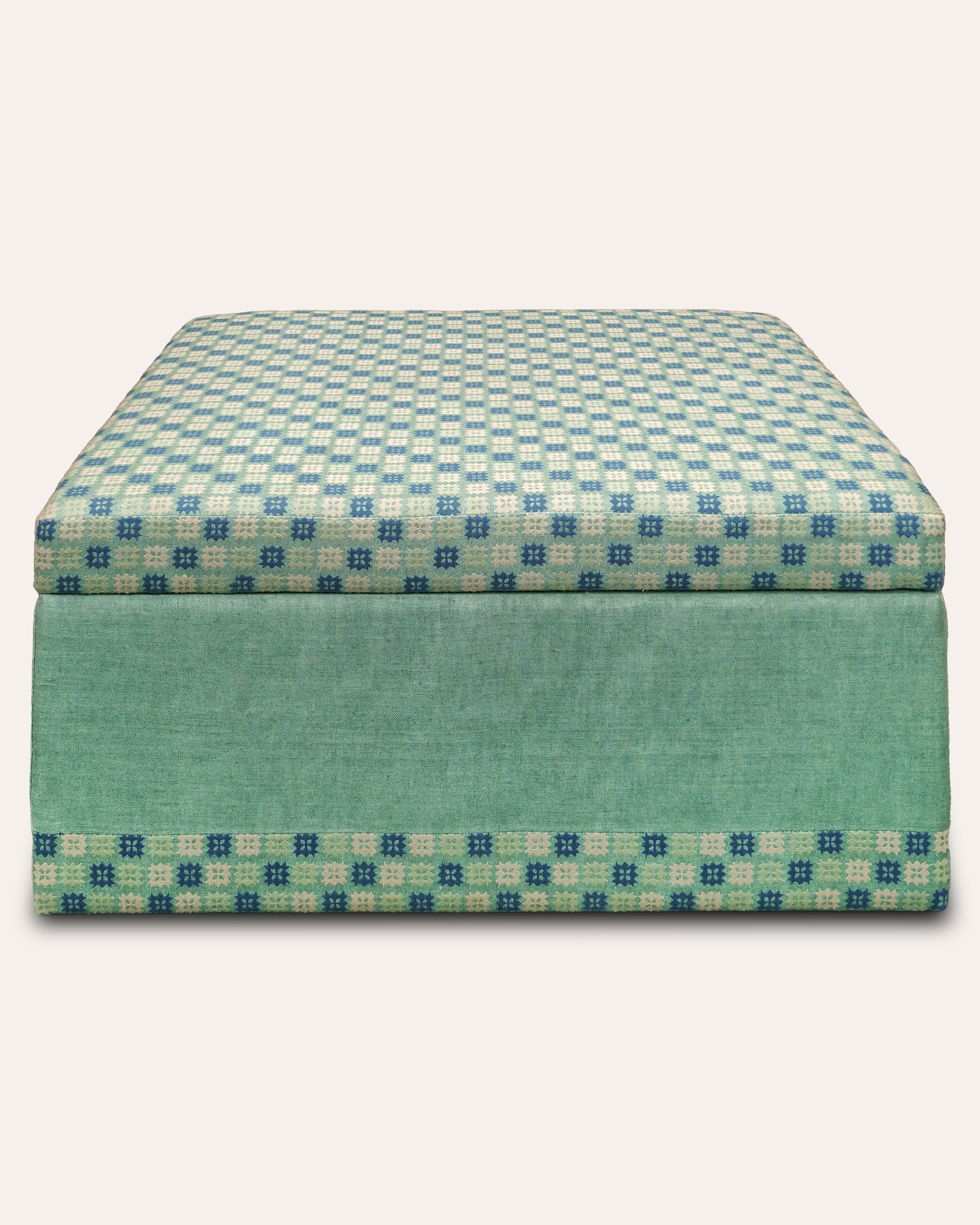 A square upholstered ottoman or storage bench with a teal and cream checkered pattern on the top and sides, and a solid teal front panel, shown against a light beige background.