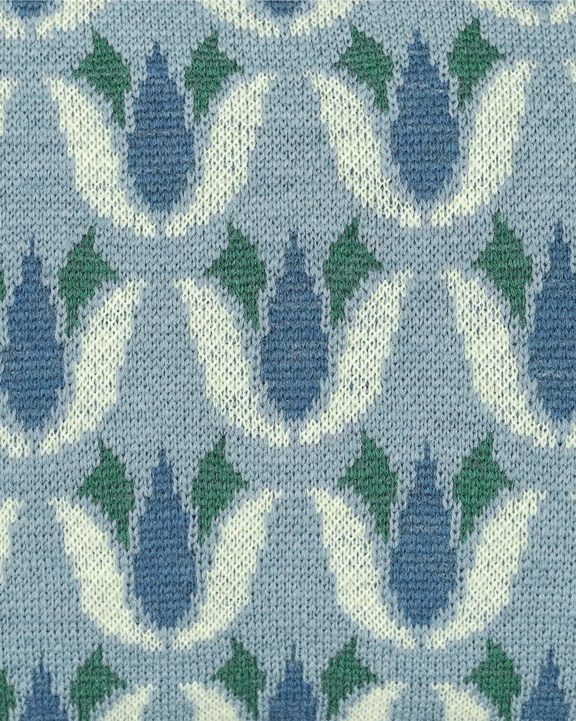 Close-up of a knitted fabric with a repeating tulip-like pattern in light blue, muted blue, green, and off-white.