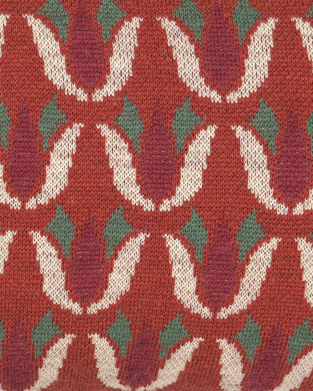 Close-up of a knitted textile with a repeating floral pattern in rust red, cream, and muted green.