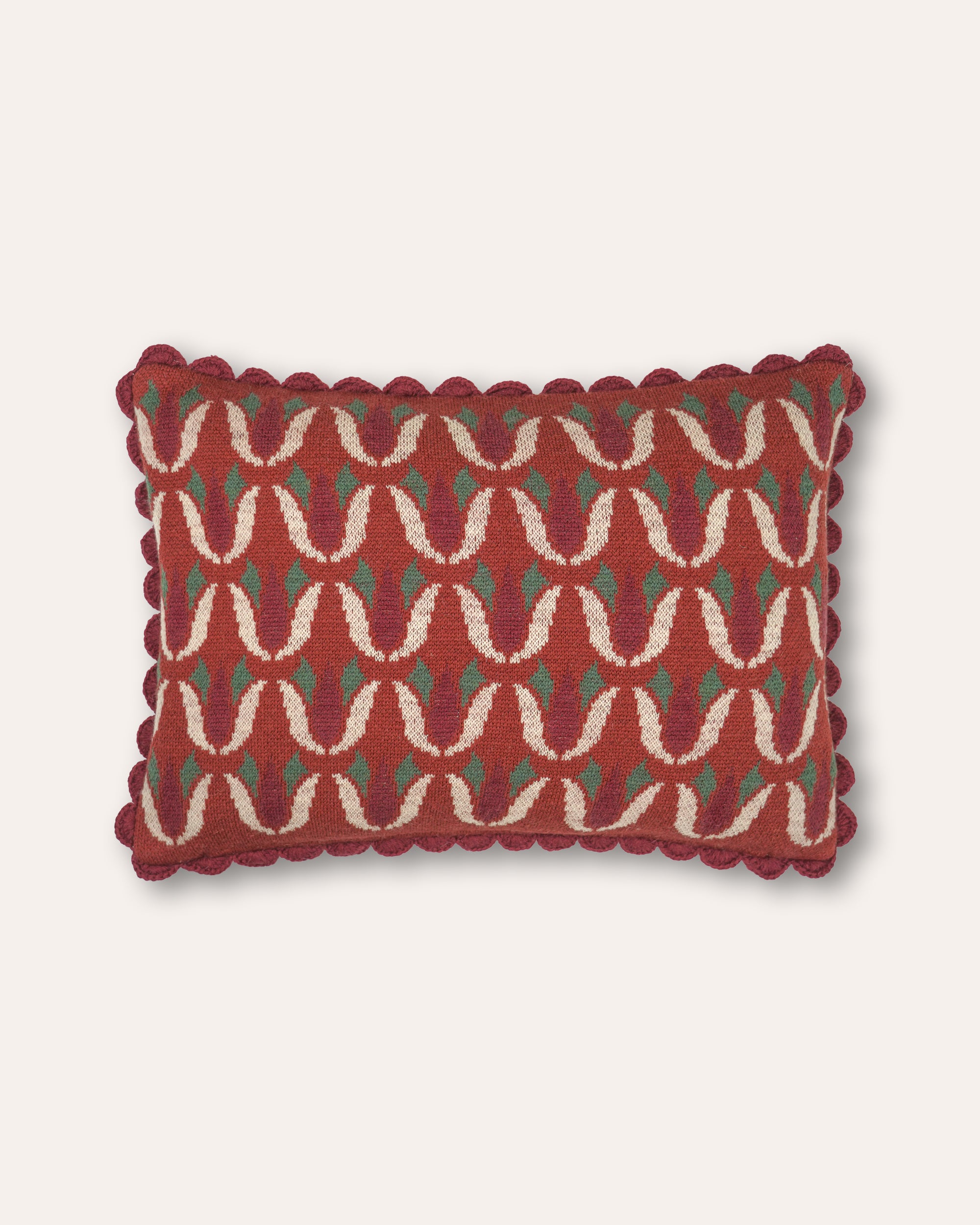 A rectangular decorative cushion with a scalloped ric-rac trim, featuring a woven geometric pattern in rust red, cream, and green on a light beige background.