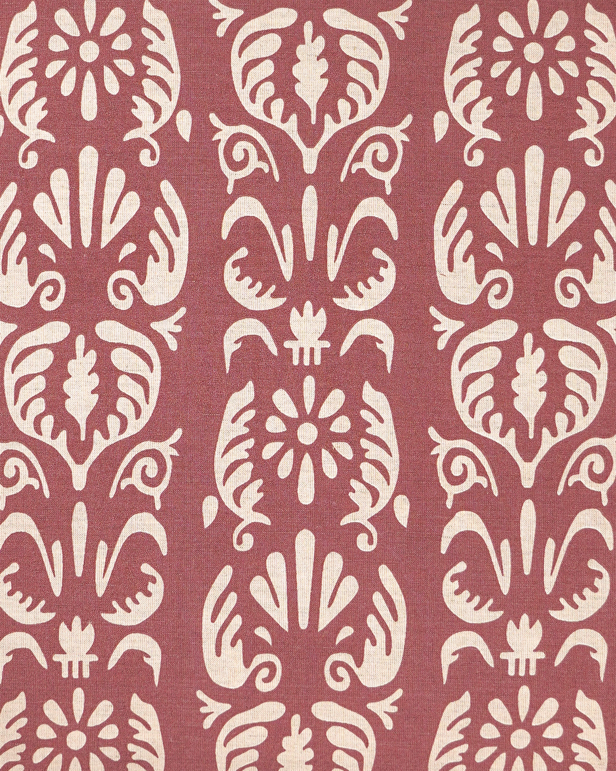 A close-up of a patterned fabric featuring a repeating vertical damask-style motif in cream on a muted dusty rose background.