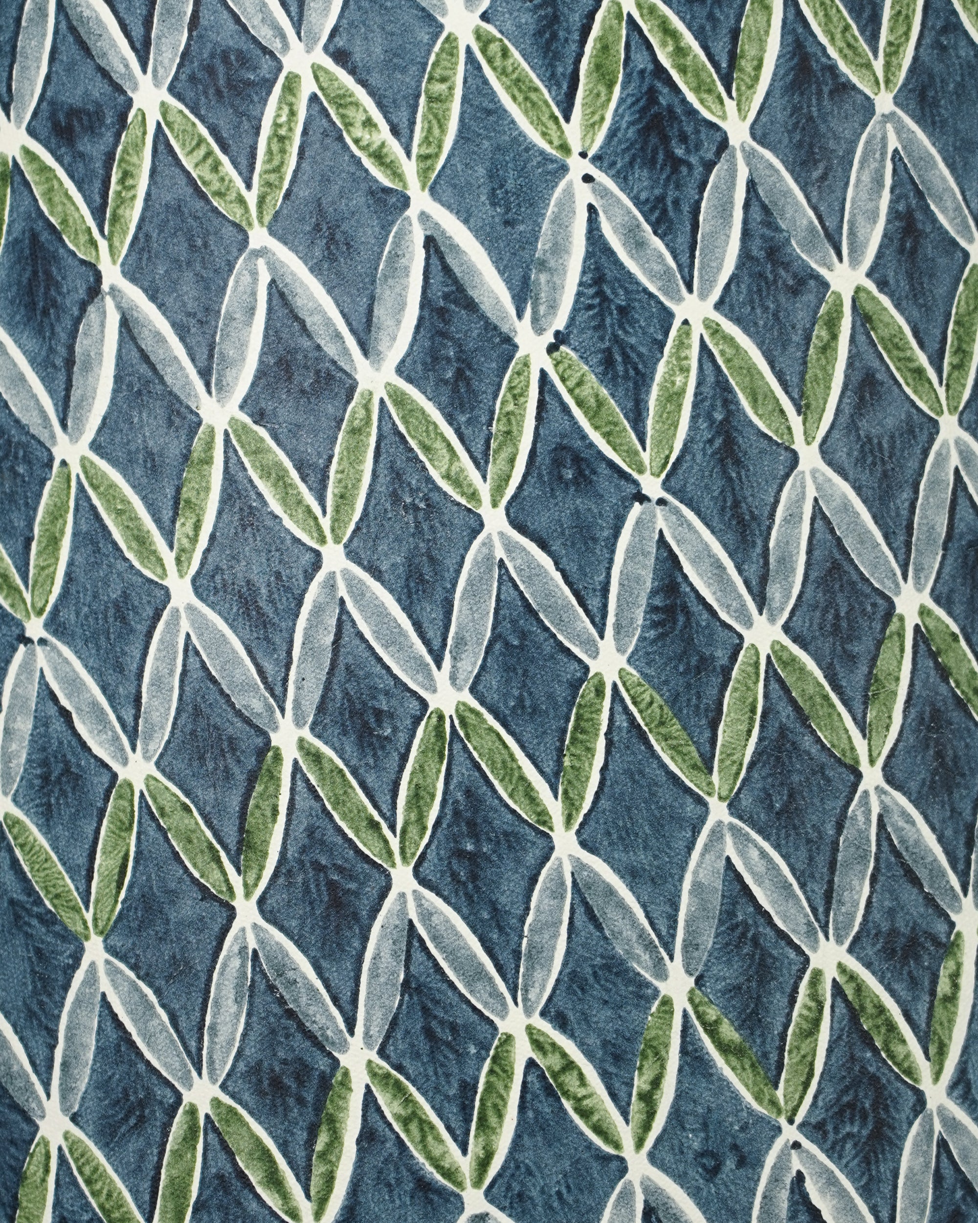 A close-up of a textured fabric featuring a repeating geometric pattern of interlocking diamond shapes in light gray, green, and blue.