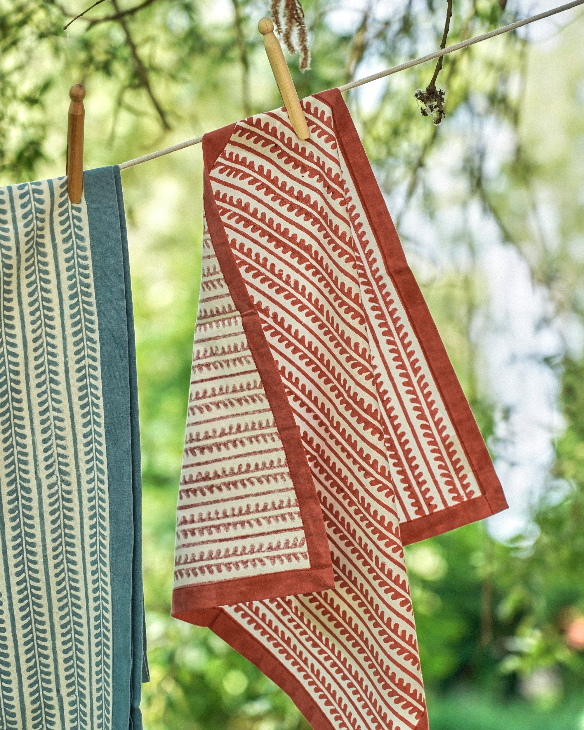 Textile with red and white pattern hanging on a clothesline against a blurred green background