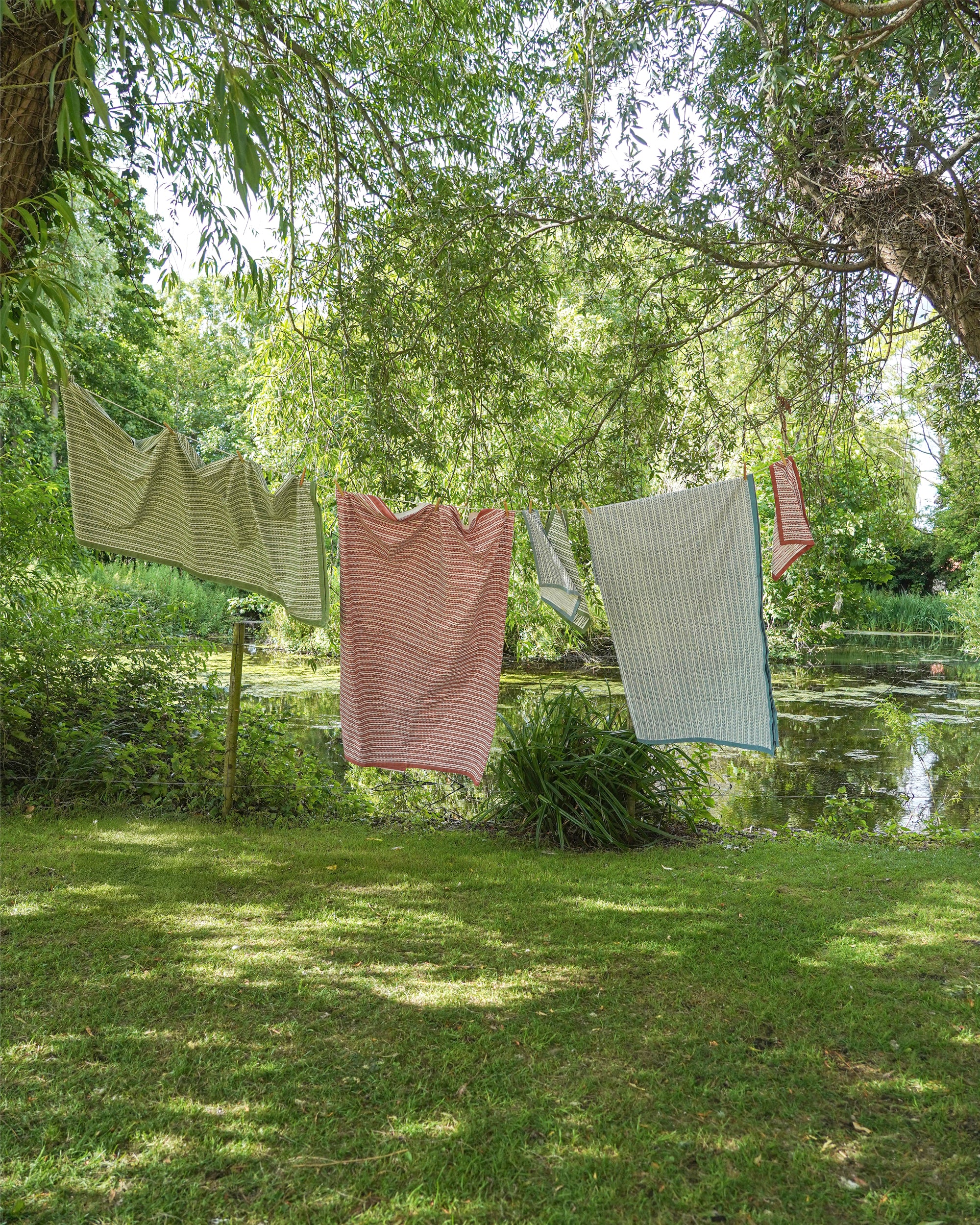 Tablecloths hanging on a clothesline in a lush green outdoor setting with trees and water in the background.
