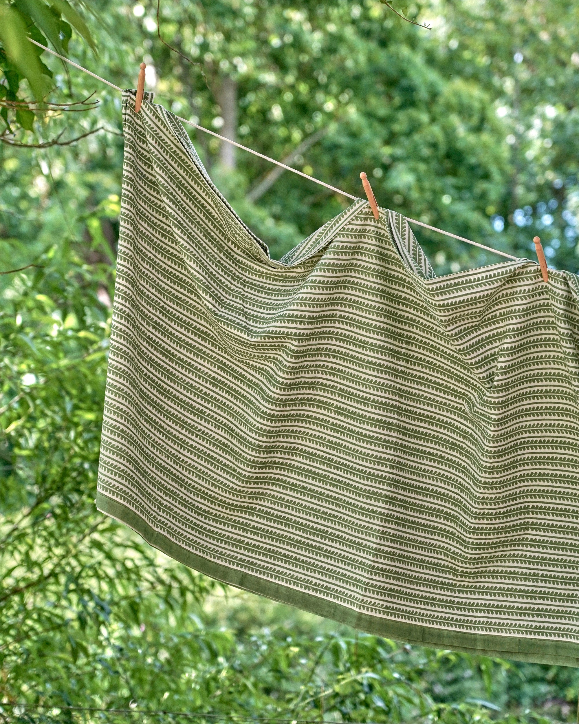 Green and white striped tablecloth hanging on a clothesline with trees in the background