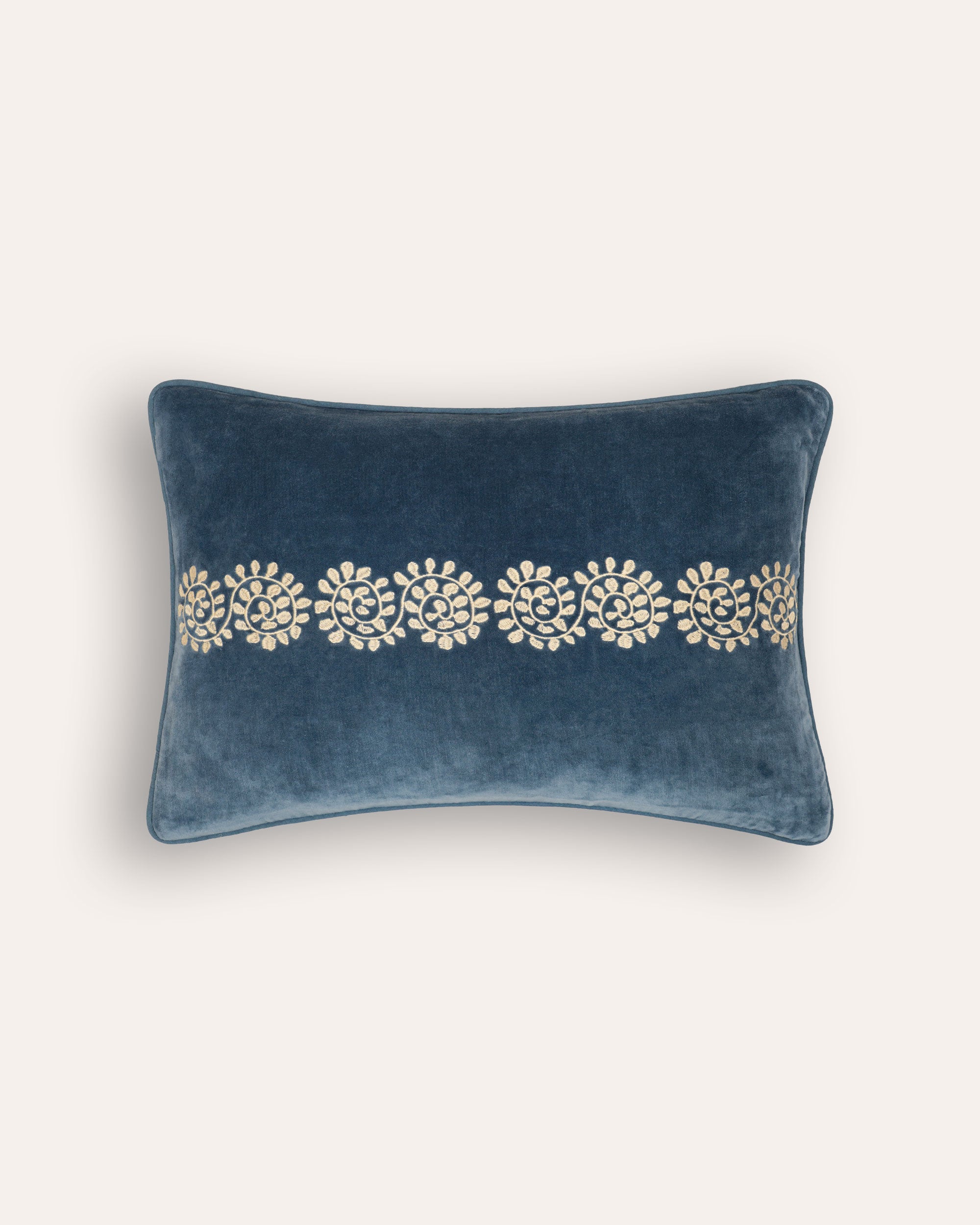 A rectangular blue velvet cushion with a floral and geometric embroidered design in the center.