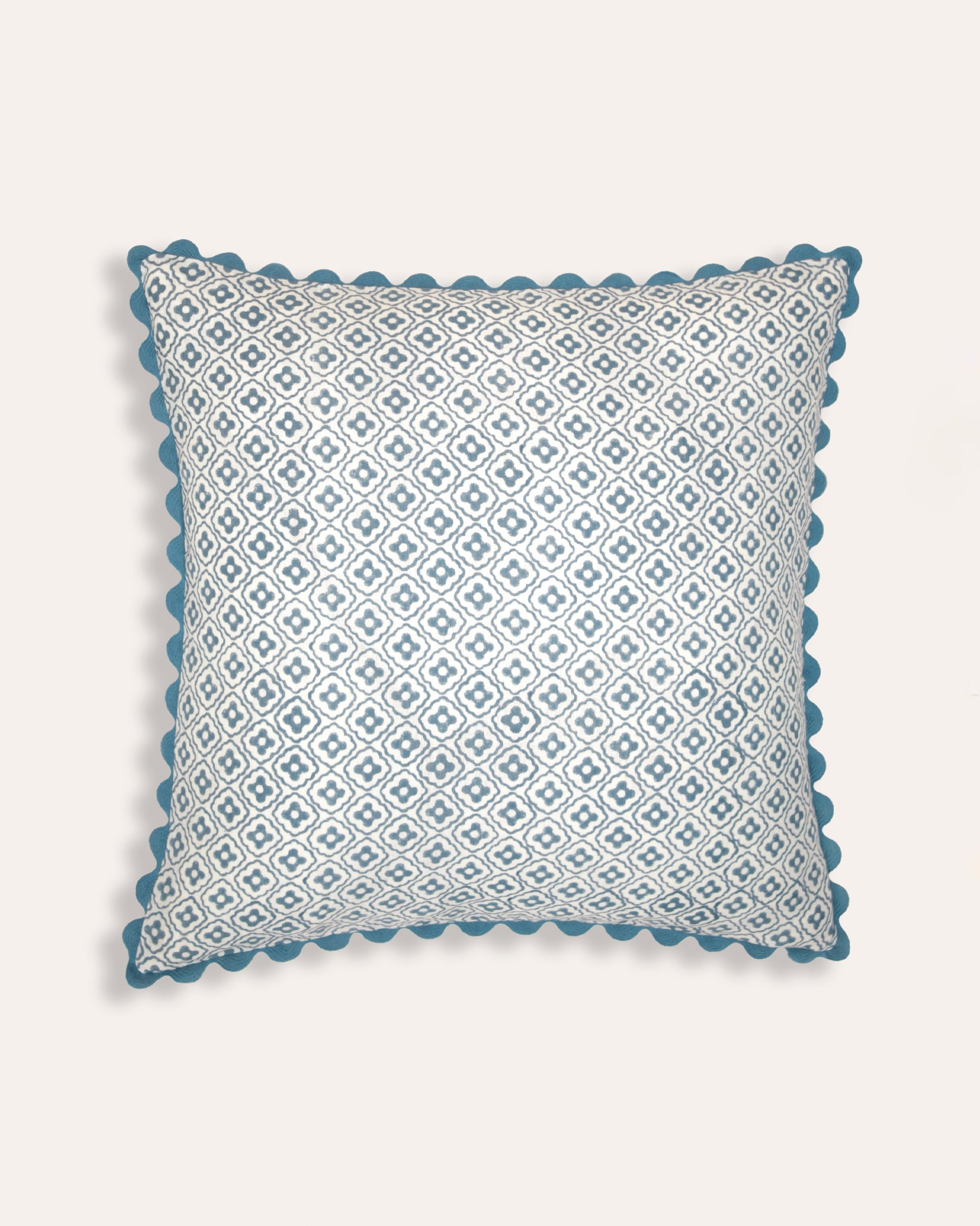 A square-shaped cushion with a blue geometric block print design and ricrac trim.