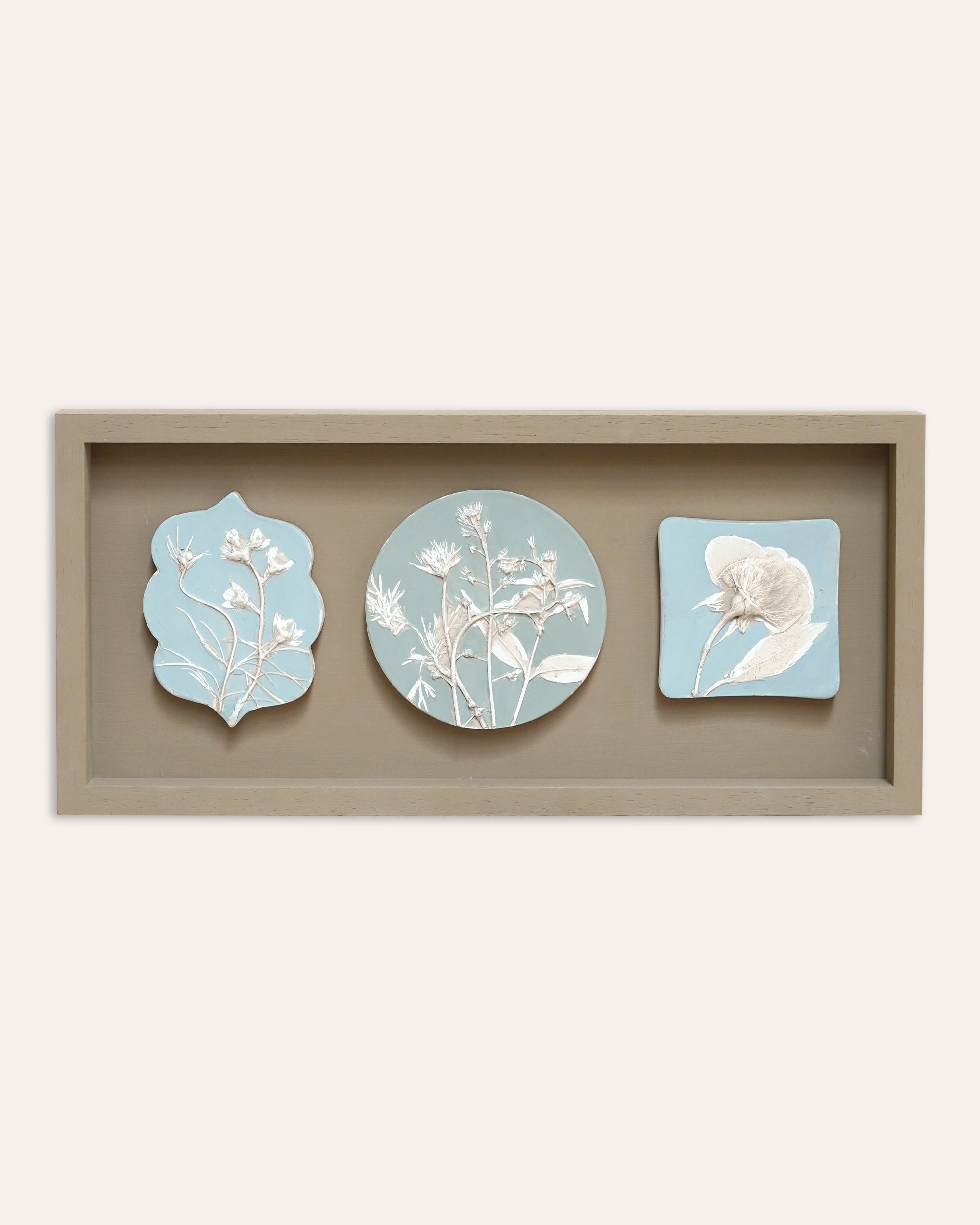 Set of three decorative casts with floral designs in a wooden frame on a white background
