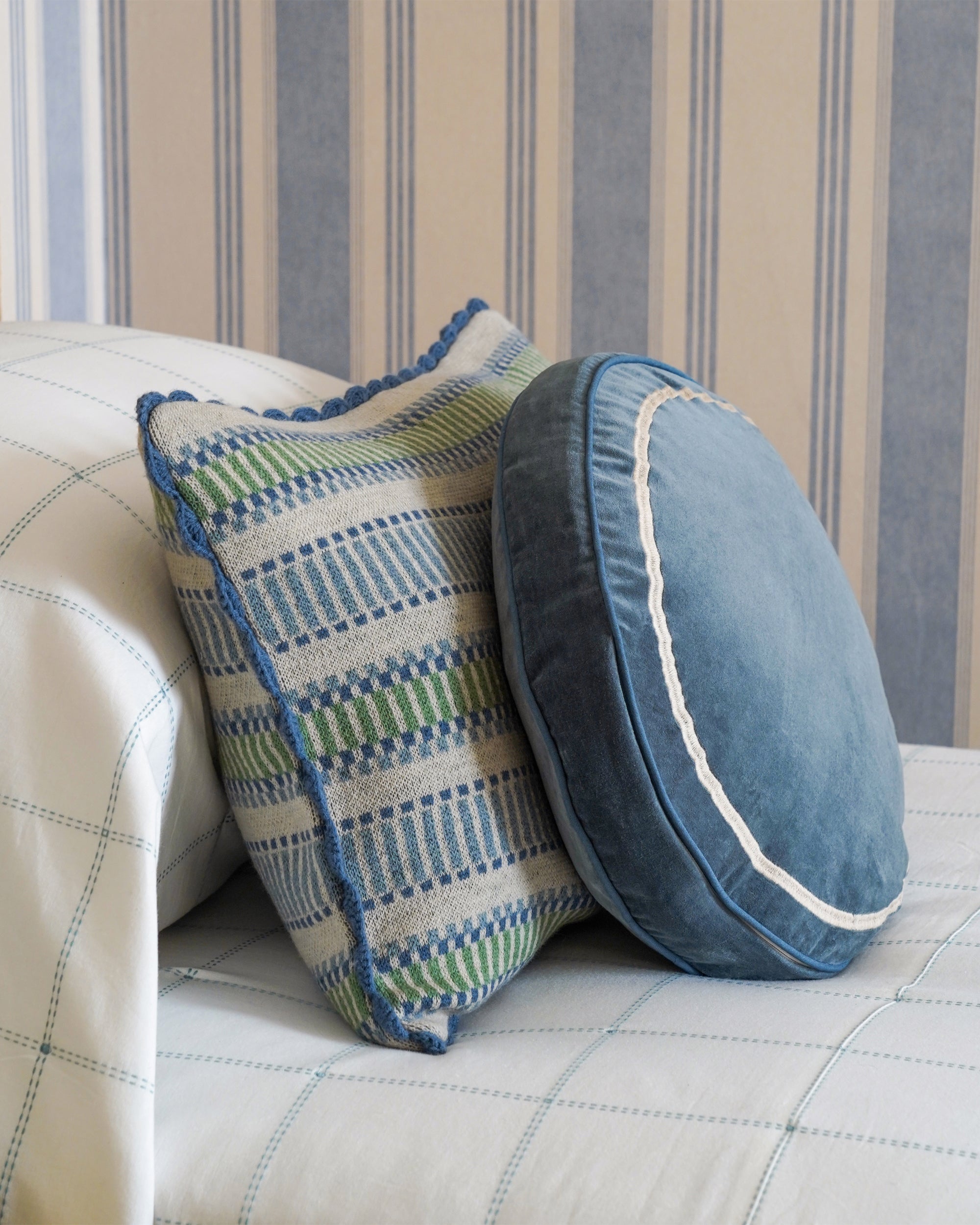 Two decorative pillows on a sofa with striped wallpaper in the background