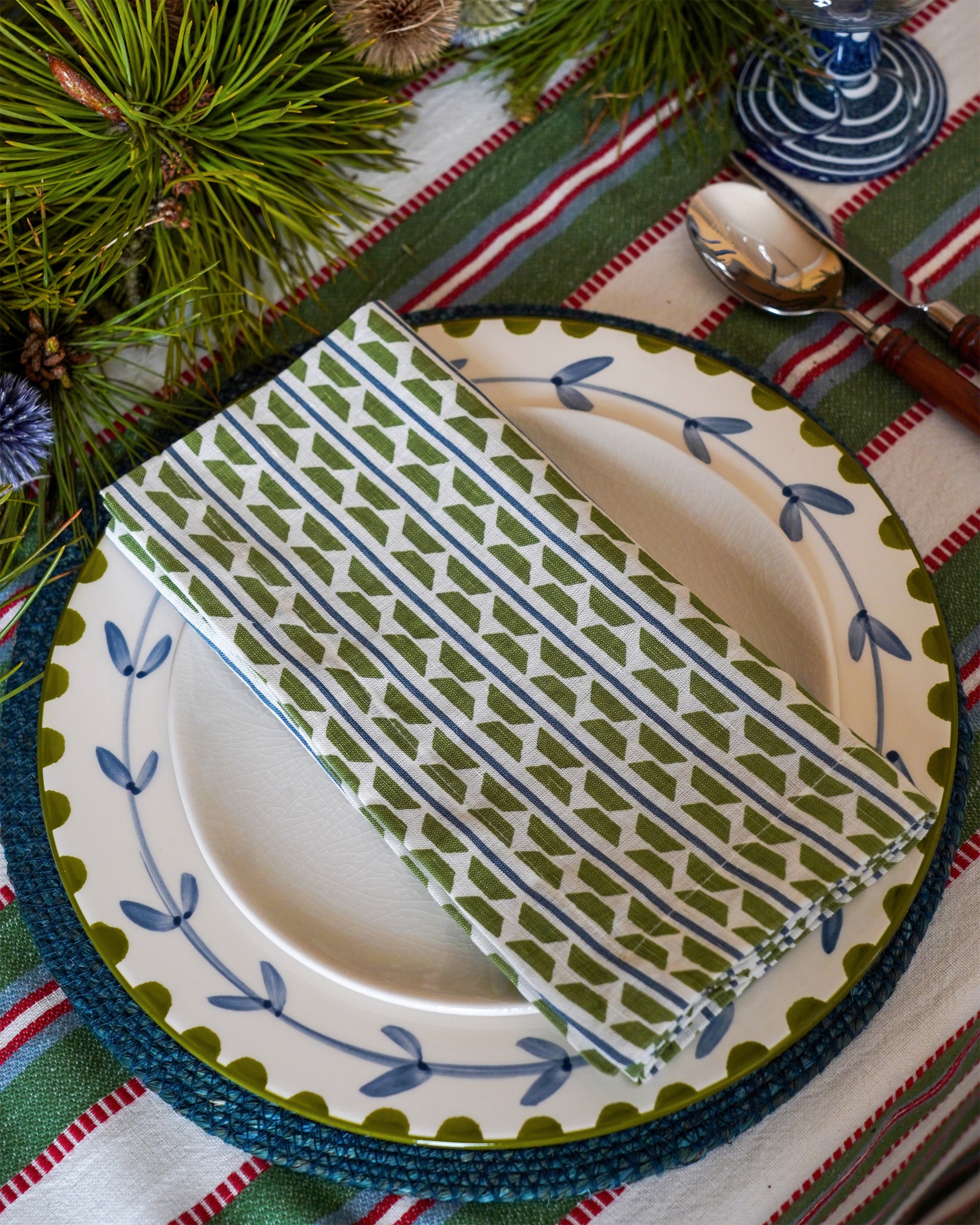 Patterned napkin on a plate with a green and red striped Colaba tablecloth and decorations.