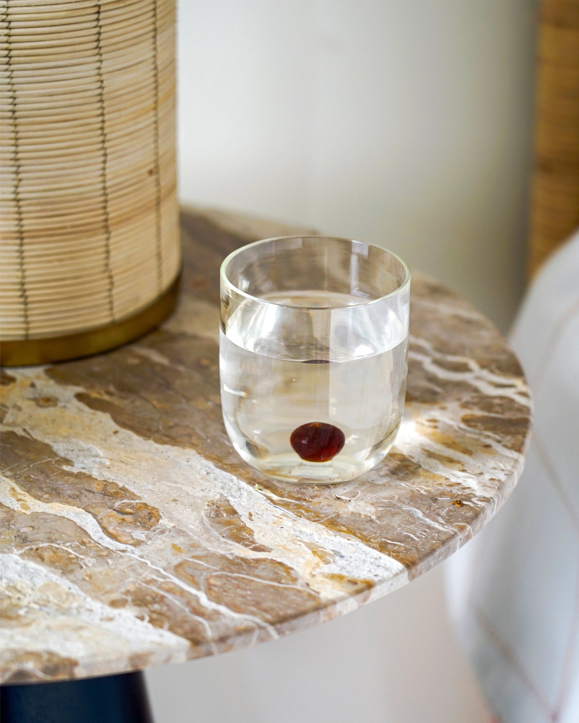 Clear glass with water and a red berry on a marble surface