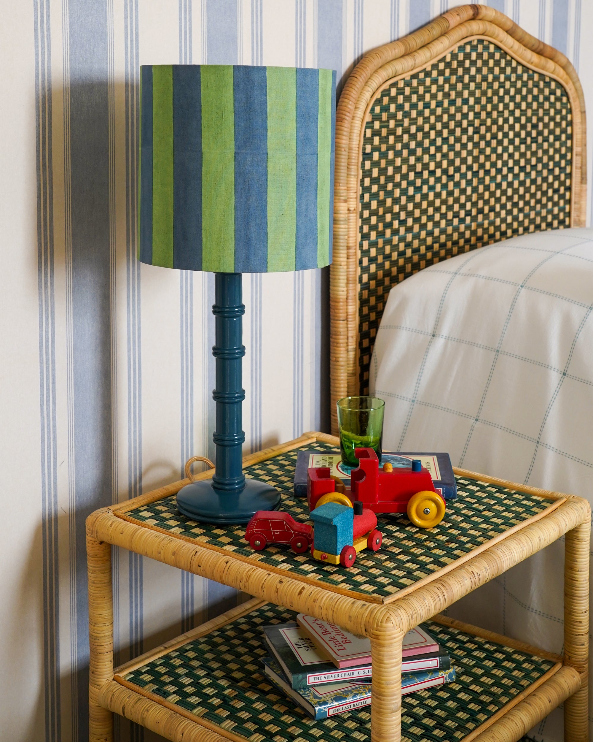 Wicker side table with colorful striped lamp and toys against a striped wall.