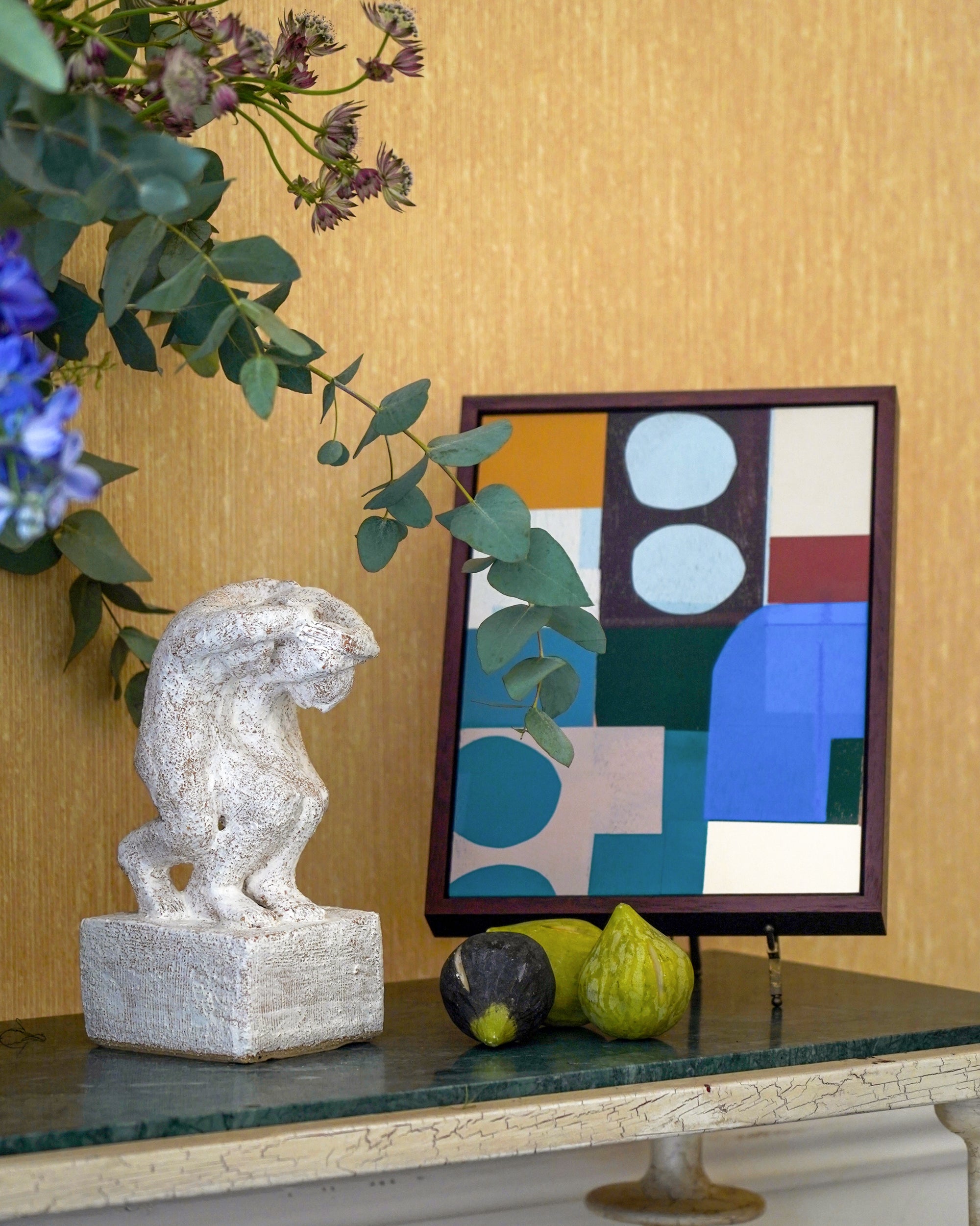 Decorative sculpture, fruits, and abstract art on a surface with a gold wall background