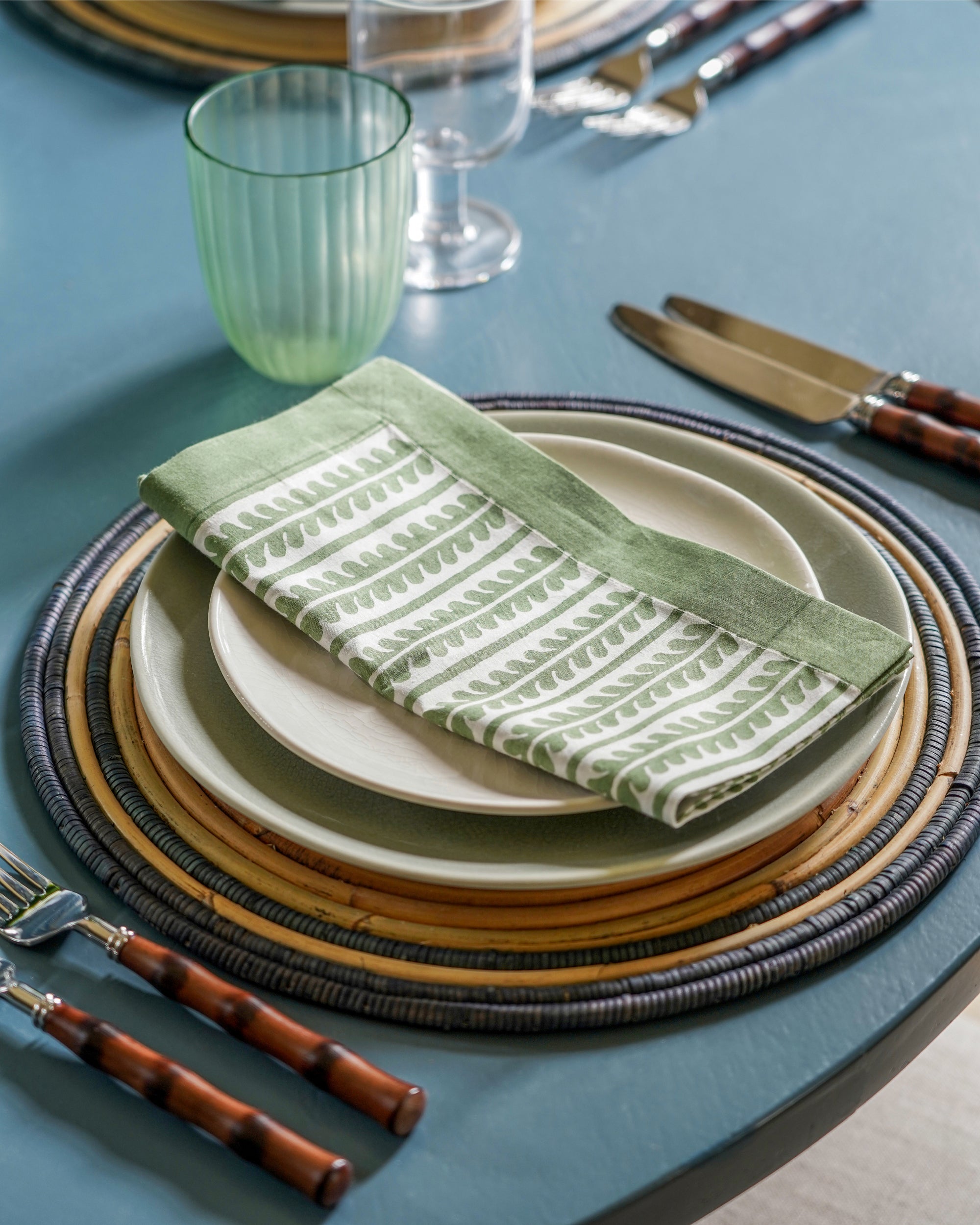 Dining table setting with green and white patterned napkin on stacked plates.