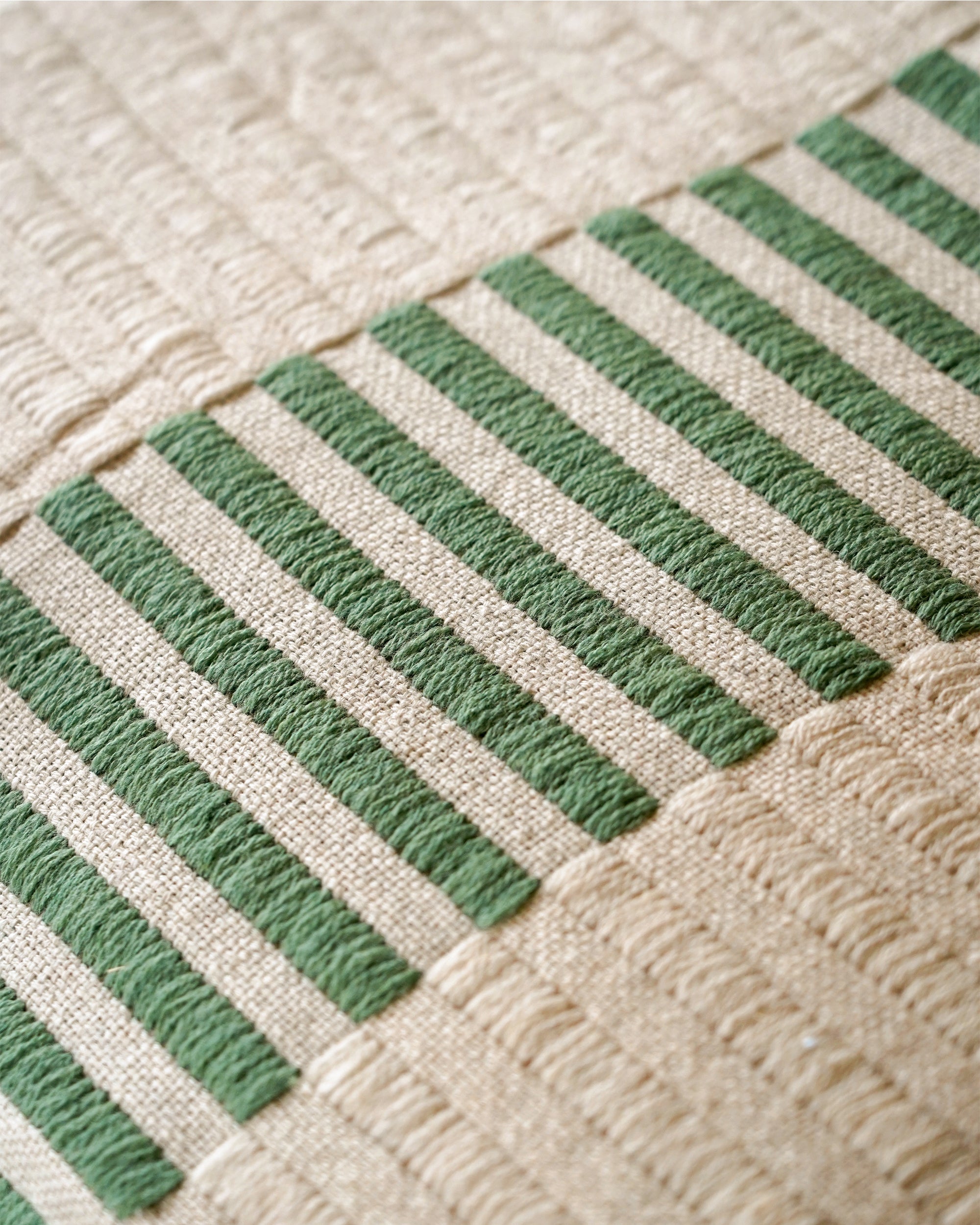Close-up of a textured fabric with green horizontal stripes on a beige background